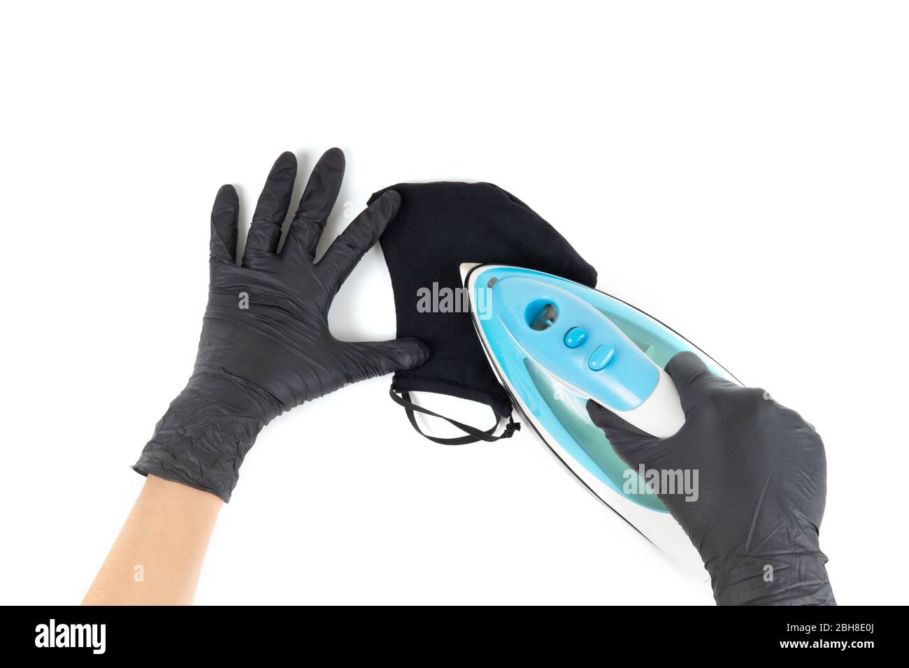 Weibliche Hände in schwarzen Einweghandschuhen bügeln eine schwarze wiederverwendbare Gesichtsmaske aus Baumwolle. Erste Person Ansicht, isoliert auf weiß. Stockfoto