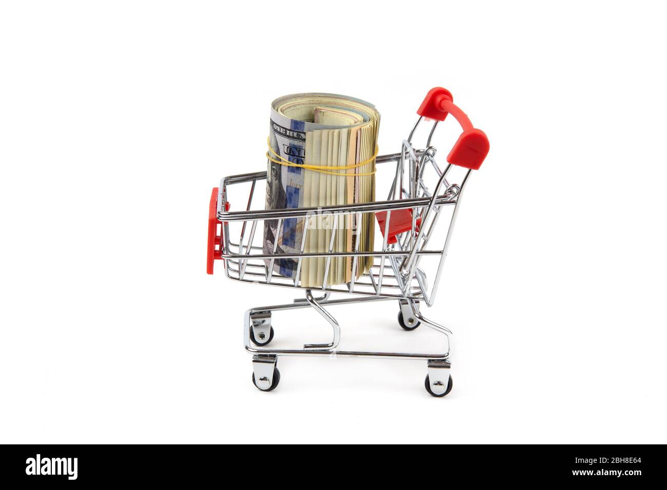 Ein Bündel von zusammengerollten Dollarscheinen in einem Miniatur-Einkaufswagen mit roten Griffen auf Weiß isoliert. Einkaufskonzept. Stockfoto