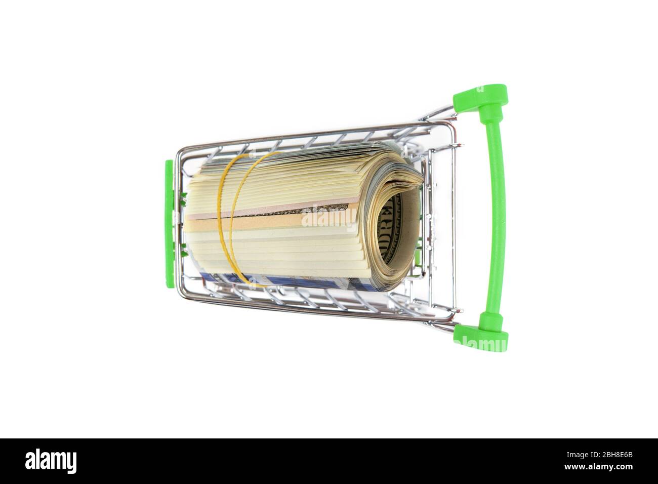 Draufsicht auf eine Rolle Dollarscheine in einem Miniatur-Lebensmittelwagen mit grünen Griffen. Nahaufnahme, isoliert auf Weiß, selektiver Fokus. Stockfoto