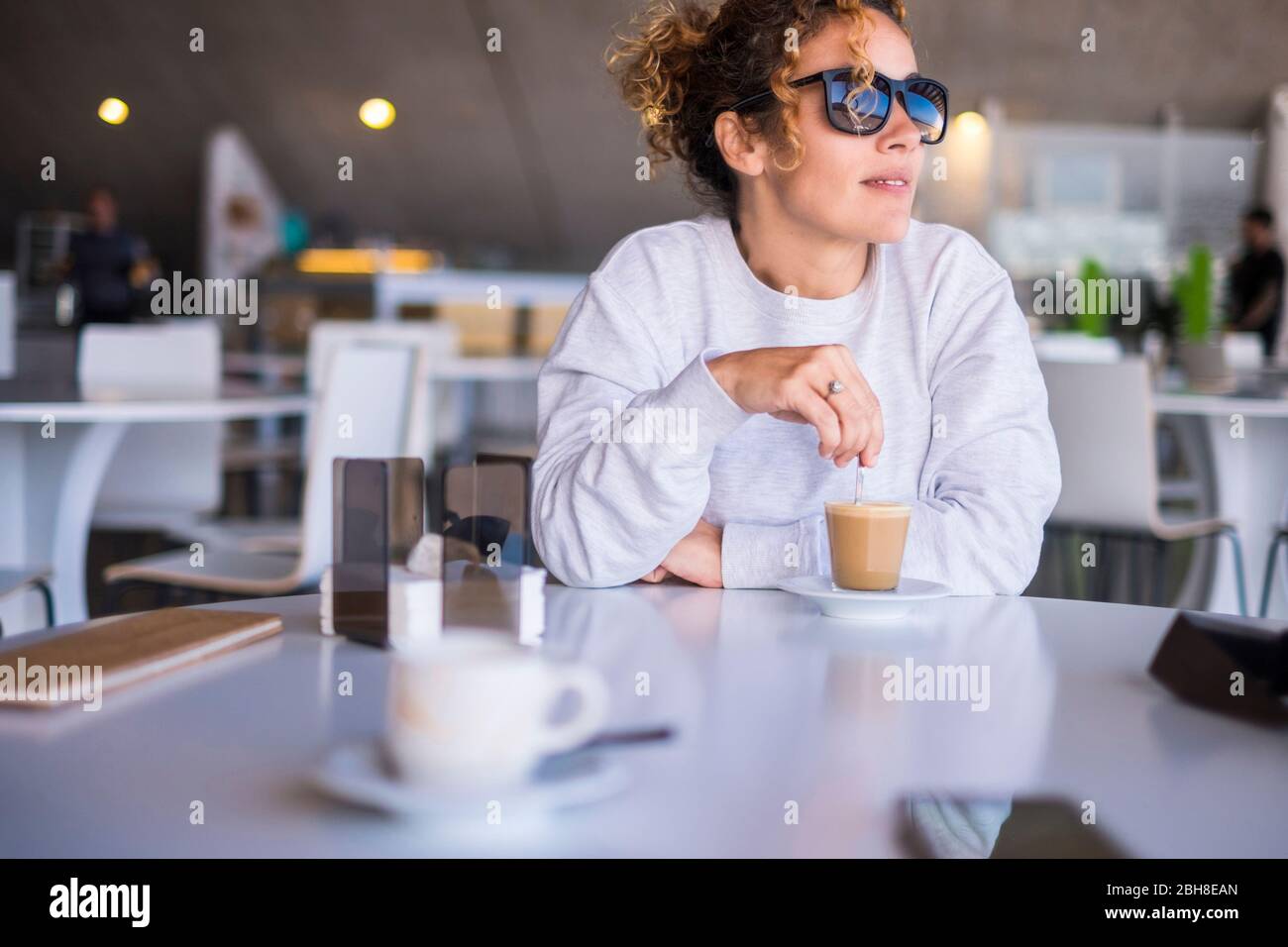 Schöne kaukasische Mittelalterfrauen mit Sonnenbrille nehmen und trinken Sie einen Kaffee in einer Bar. Außenlicht aus Fenster für eine Freizeit Ruhetag während des Tages. Ruhig und entspannen Stockfoto