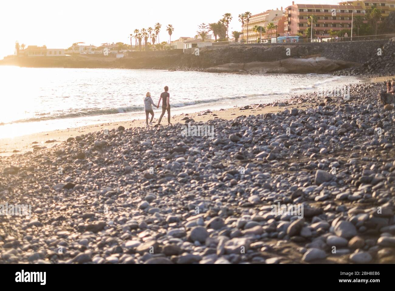 Romantisches Paar zu Fuß am Strand in der Nähe von Wellen und Flut. Felsen Strand für Familie und Menschen in der Liebe mit goldenen Sonnenuntergang im Hintergrund Stockfoto