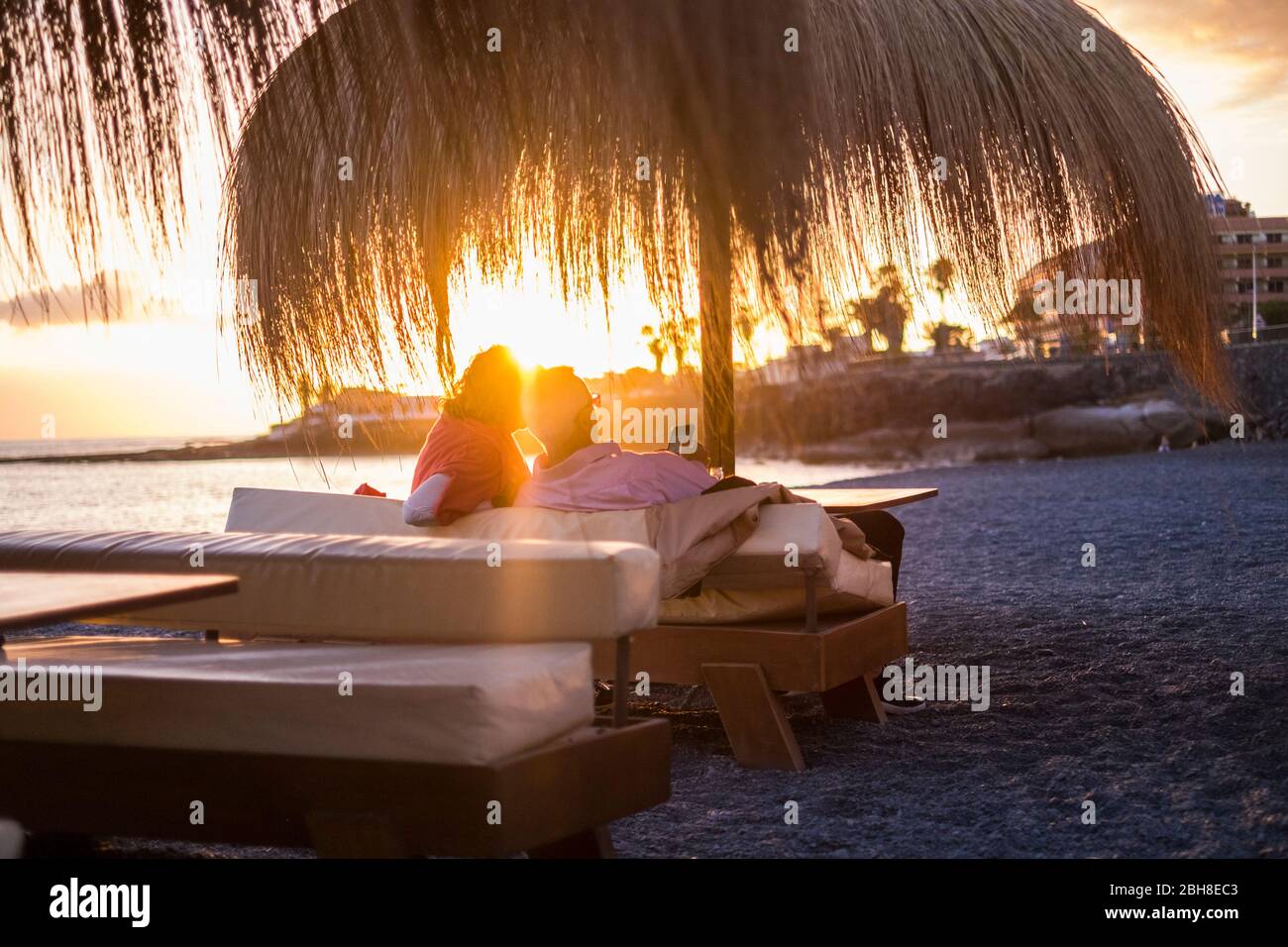 Romantische Szene mit Sonnenuntergang für ältere Erwachsene Paar sitzen und genießen Cocktail im Urlaub am Strand mit Meerblick. goldene Töne für Süße und Zartheit Konzept Stockfoto