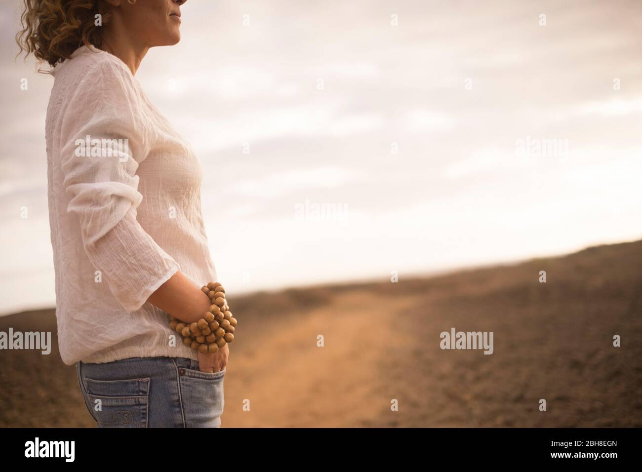 Schöne Dame mittleren Alters in der Mode legere Kleidung wie Jeans und weißem Kleid mit großen hölzernen Armband mit Wüste im Hintergrund - Stockfoto