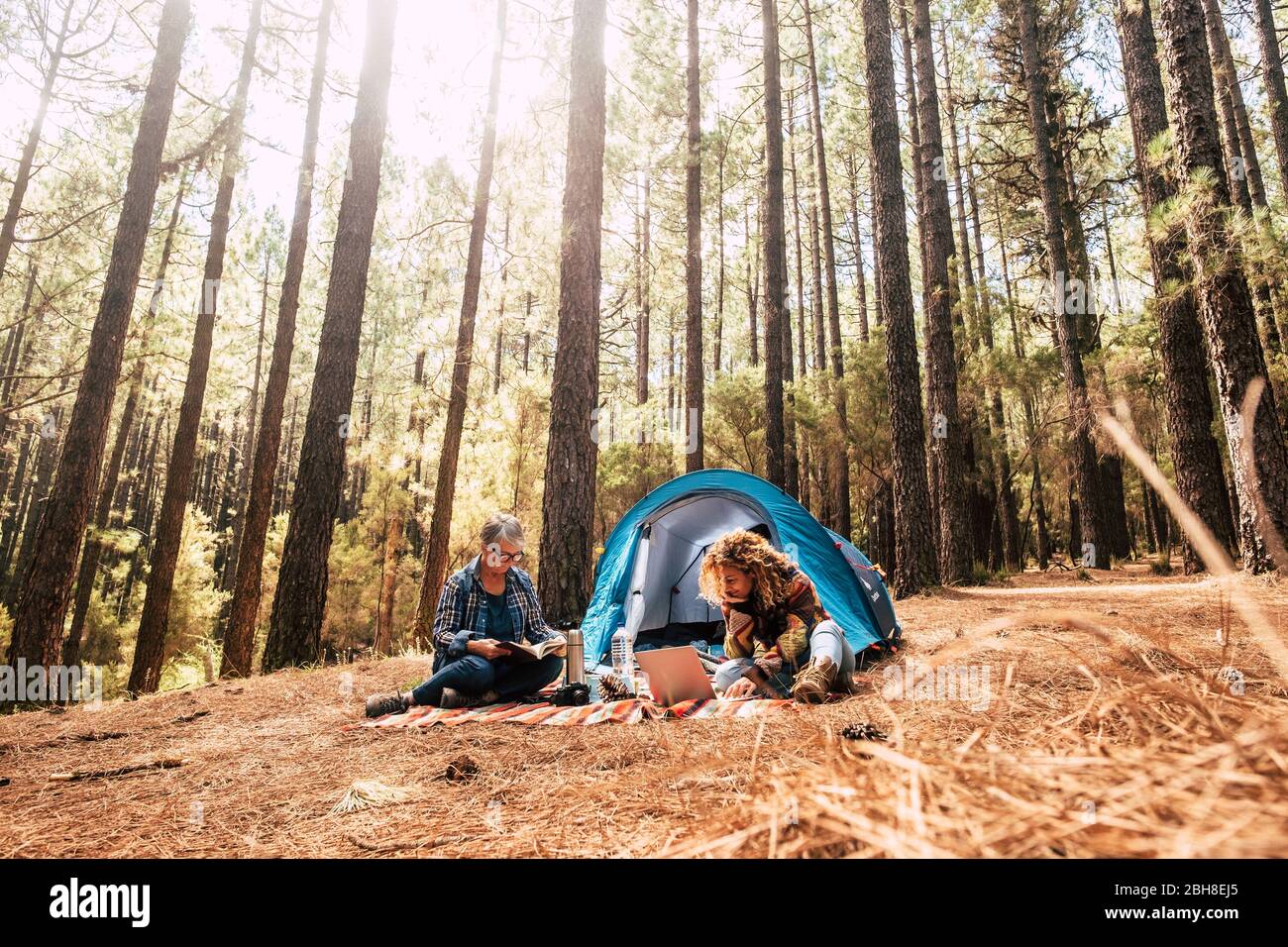 Zwei verschiedene Altersgruppen kaukasische Frau in freien Camping zusammen im Kiefernwald essen ein Sandwich - Freiheit und Unabhängigkeit für Erwachsene Menschen - alternative Büro für freiberufliche Schriftsteller Blogger Fotograf Stockfoto