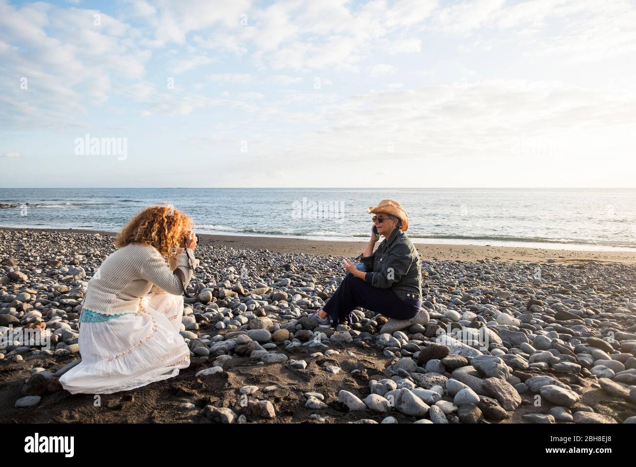 Fotoshooting mit zwei Frauen. Eine Fotografin und eine reife Frau sprechen am Telefon am Strand Stockfoto