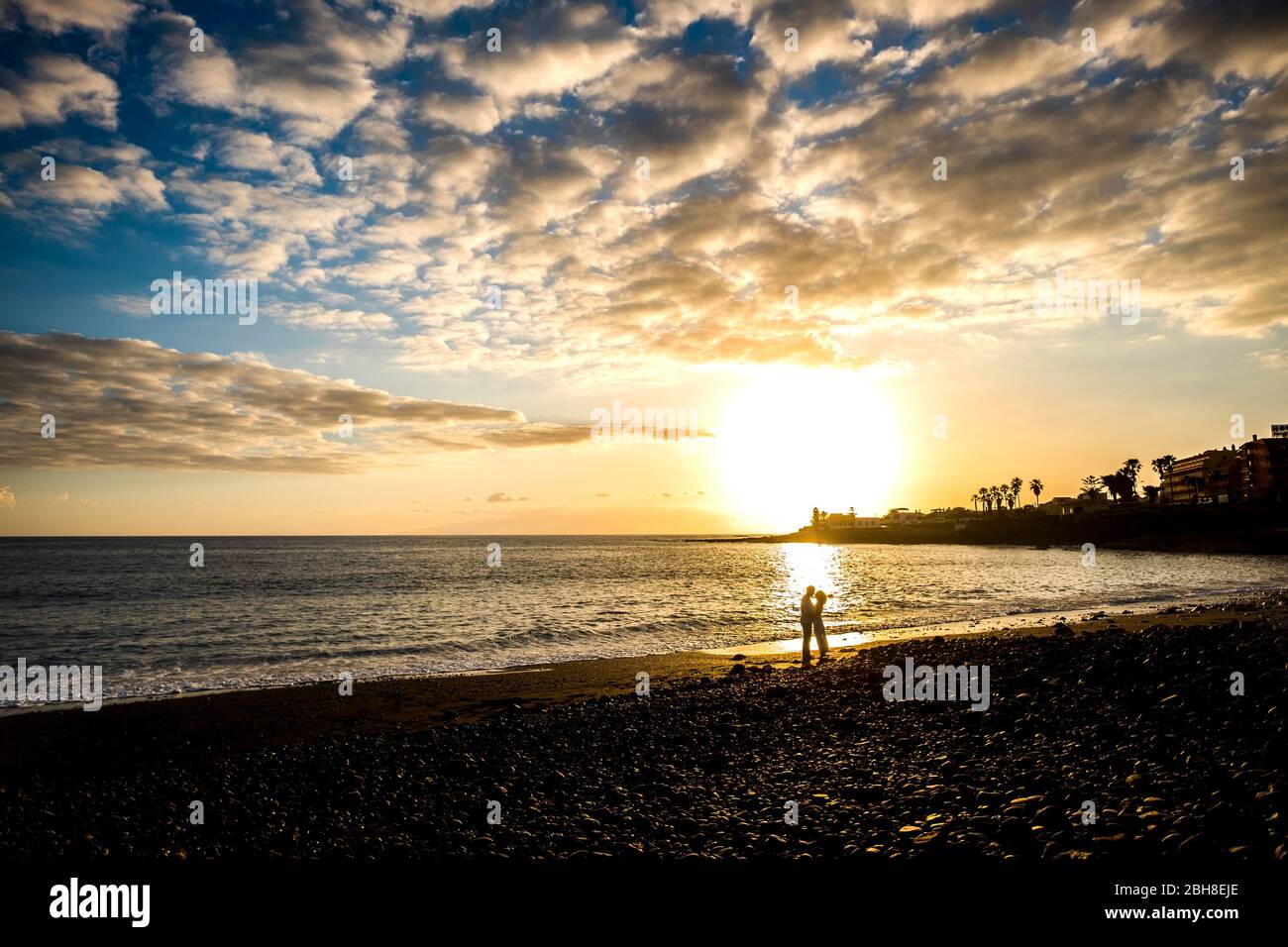Liebespaar küssen mit goldenem Sonnenuntergang im Hintergrund. Strand und Meereswellen landschaftlich schöner Ort auf Teneriffa. Romantik und Zärtlichkeit Konzept für Mann und Frau im Urlaub Stockfoto