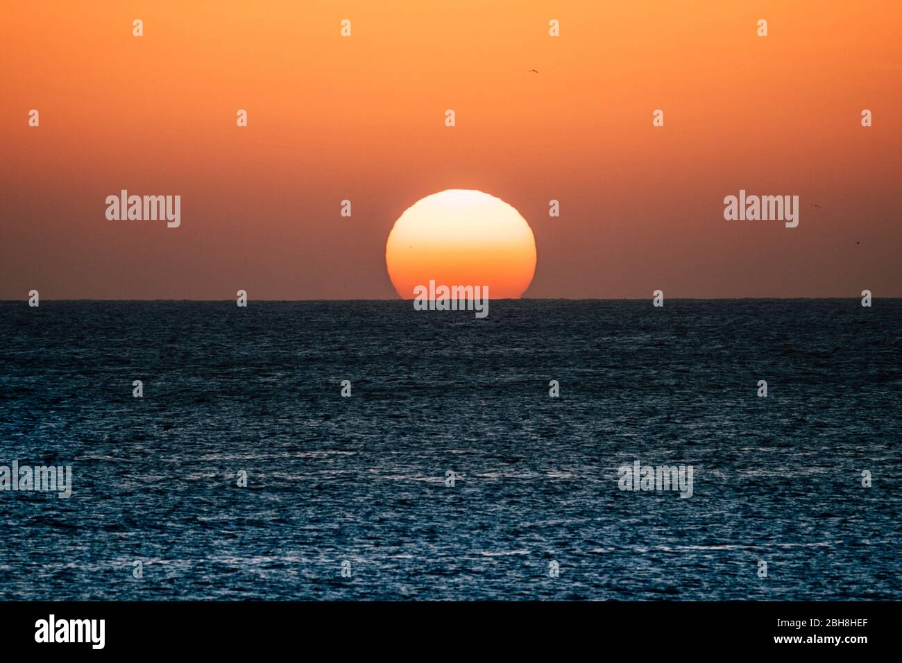 Sonnenuntergang oder Sonnenaufgang Moment über dem Meer mit Sonne, die die Horizontlinie auf dem Wasser berührt - romantisches und touristisches Konzept für Reiseurlaub Hintergrund gefärbt Stockfoto