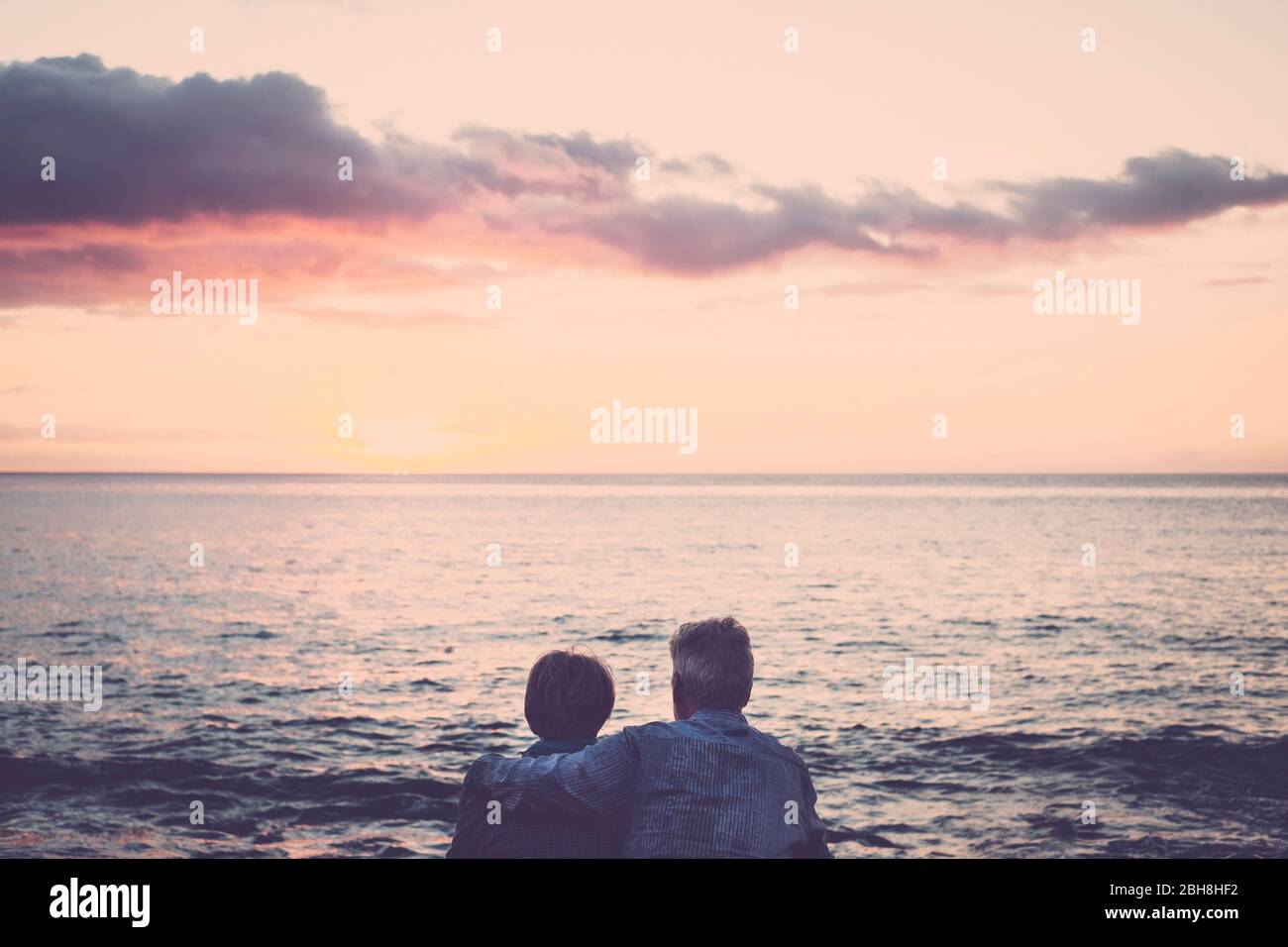 Ältere Paare sitzen und umarmen einander Blick auf das Meer bei Sonnenuntergang entspannend. Konzept von Urlaub, Freizeit, Entspannung. Liebe für kaukasische Erwachsene Menschen zusammen mit Umarmung und Beziehung Lifestyle Outdoor-Konzept Stockfoto