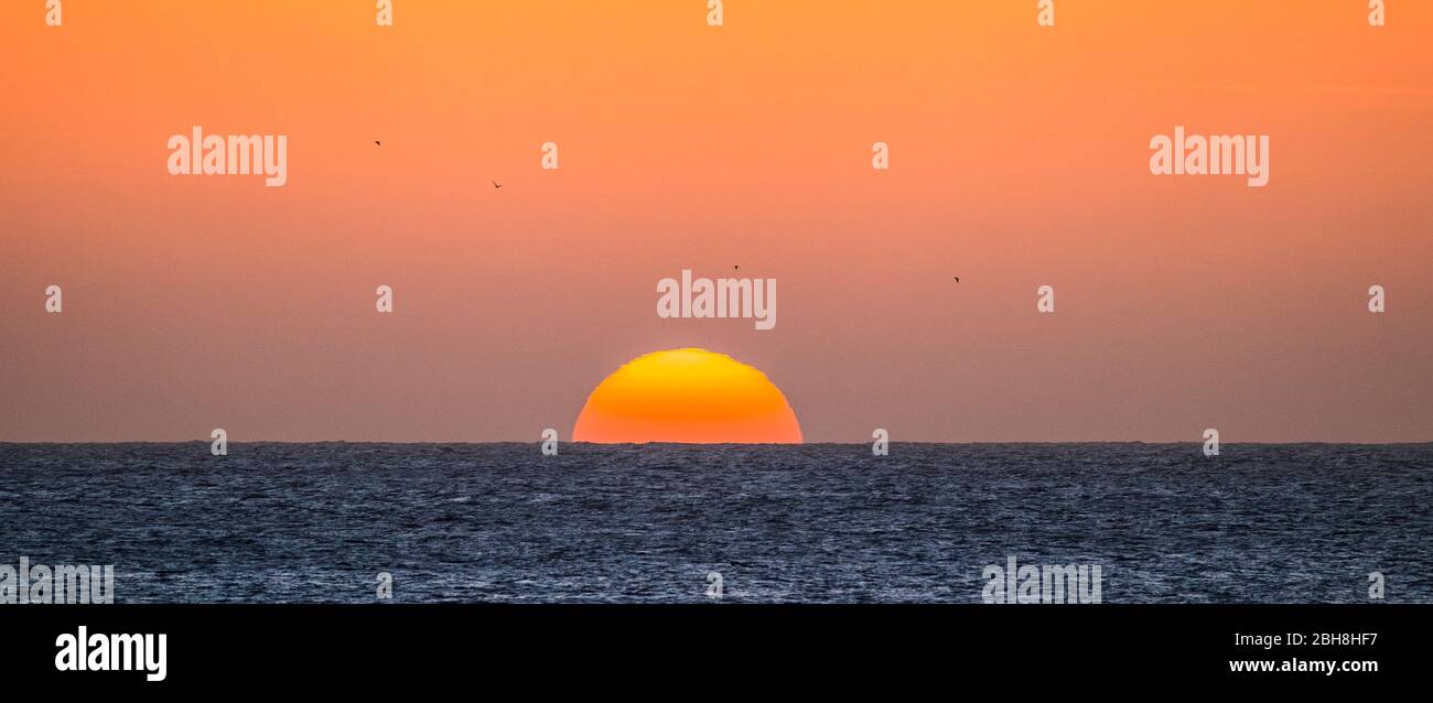 Sonnenuntergang oder Sonnenaufgang Moment über dem Meer mit Sonne, die die Horizontlinie auf dem Wasser berührt - romantisches und touristisches Konzept für Reiseurlaub Hintergrund gefärbt Stockfoto