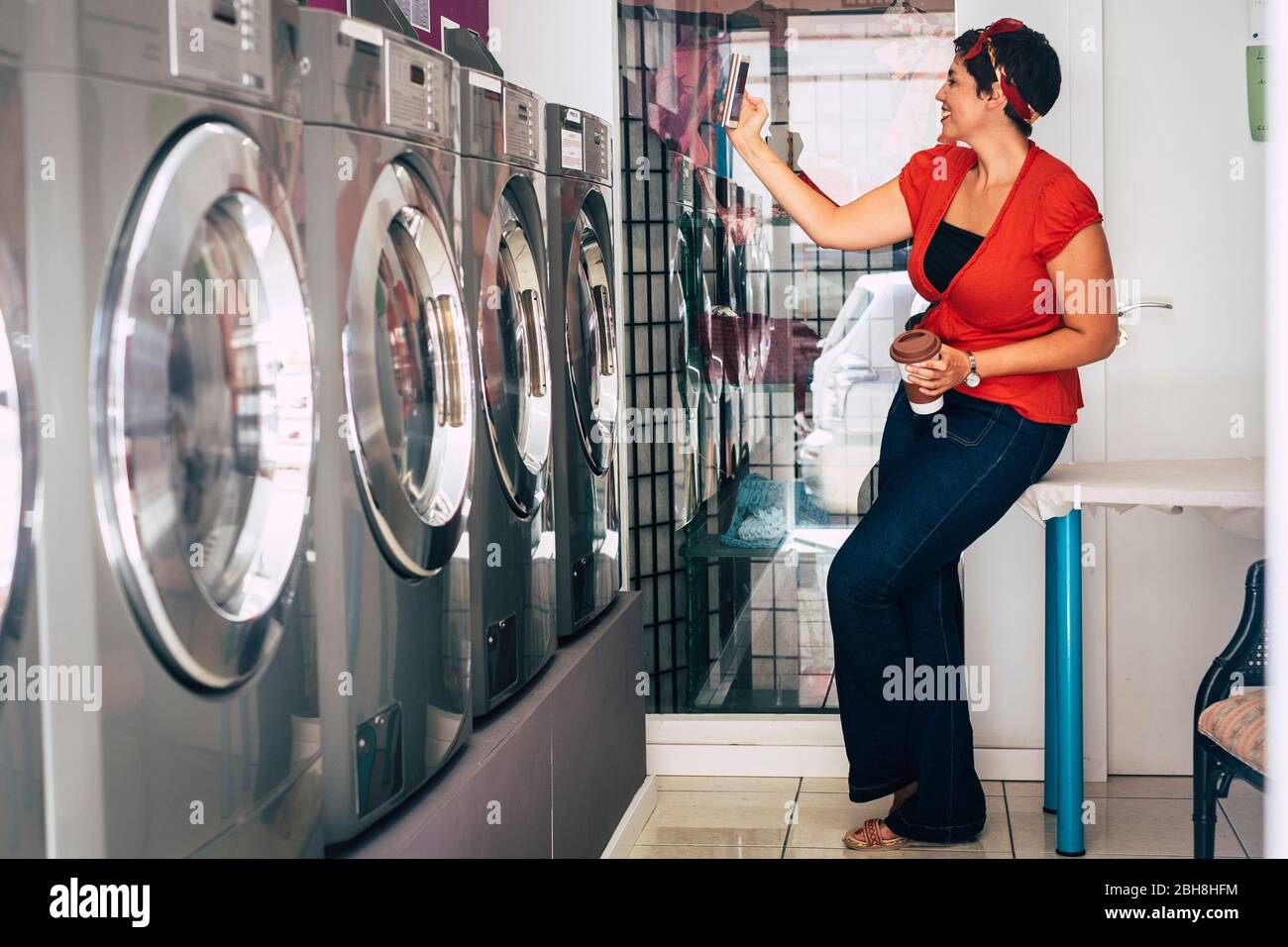 Nette Dame mit rotem Hemd genießen Technologie mit Smartphone während automatische Wäsche waschen und trocknen ihre Kleidung - modernen Lebensstil ofr Urban girl Stockfoto