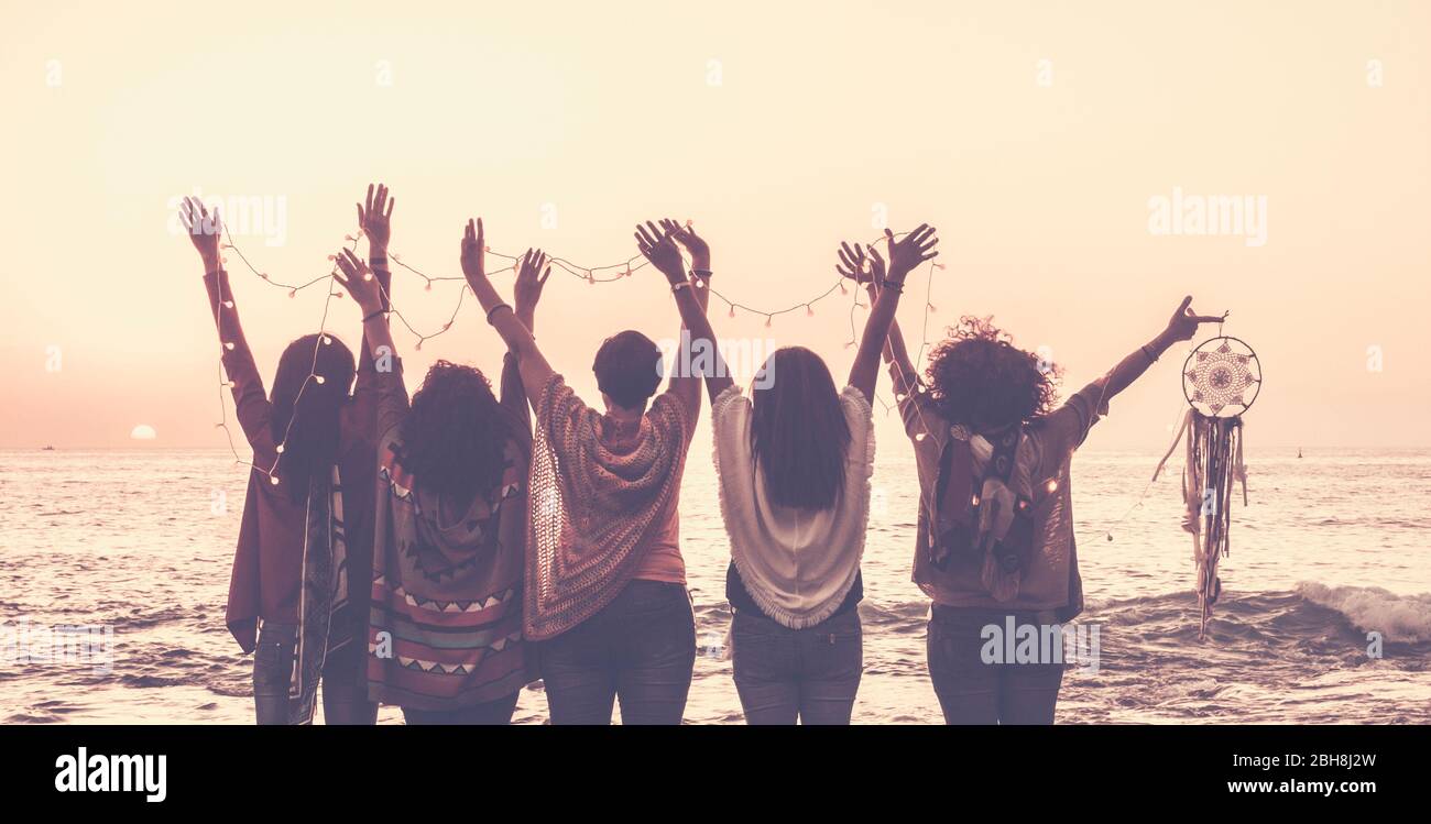 Vintage Tones Bilder von fünf Frauen Freunde von hinten gesehen aufgeben Hände für Glück vor einem Sonnenuntergang auf dem Meer und halten Lichter und ein Traumfänger für spirituelle Konzept Stockfoto