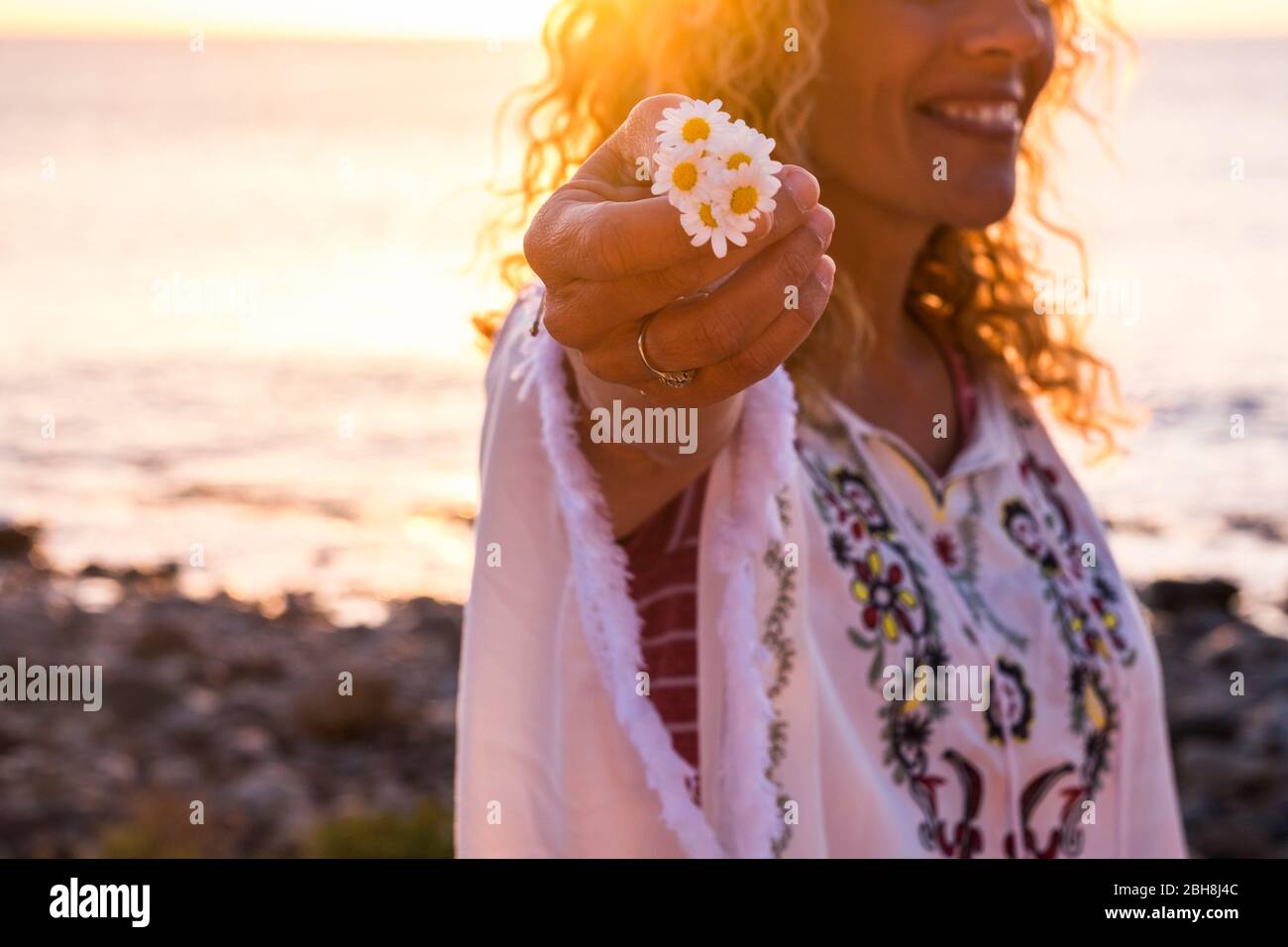 Fröhlich glücklich freee kaukasischen mittleren Alters Frau in Hippie Mode Kleidung nehmen eine schöne Gänseblümchen Blume - Fokus auf Blumen und Sonne Hintergrundbeleuchtung - Sonnenuntergang im Hintergrund für das Leben zu genießen Konzept Stockfoto
