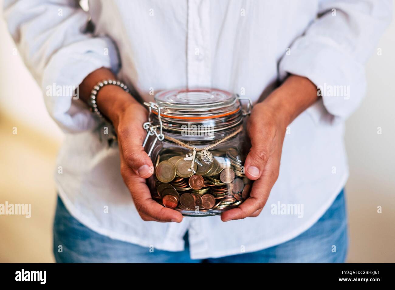 Nahaufnahme der Hände der Frau zu Hause mit einer transparenten Glasvase voller Münzen und Flugzeug draußen - Wirtschaft und Geld für den nächsten Urlaub - vertrautes Geschäftskonzept Stockfoto