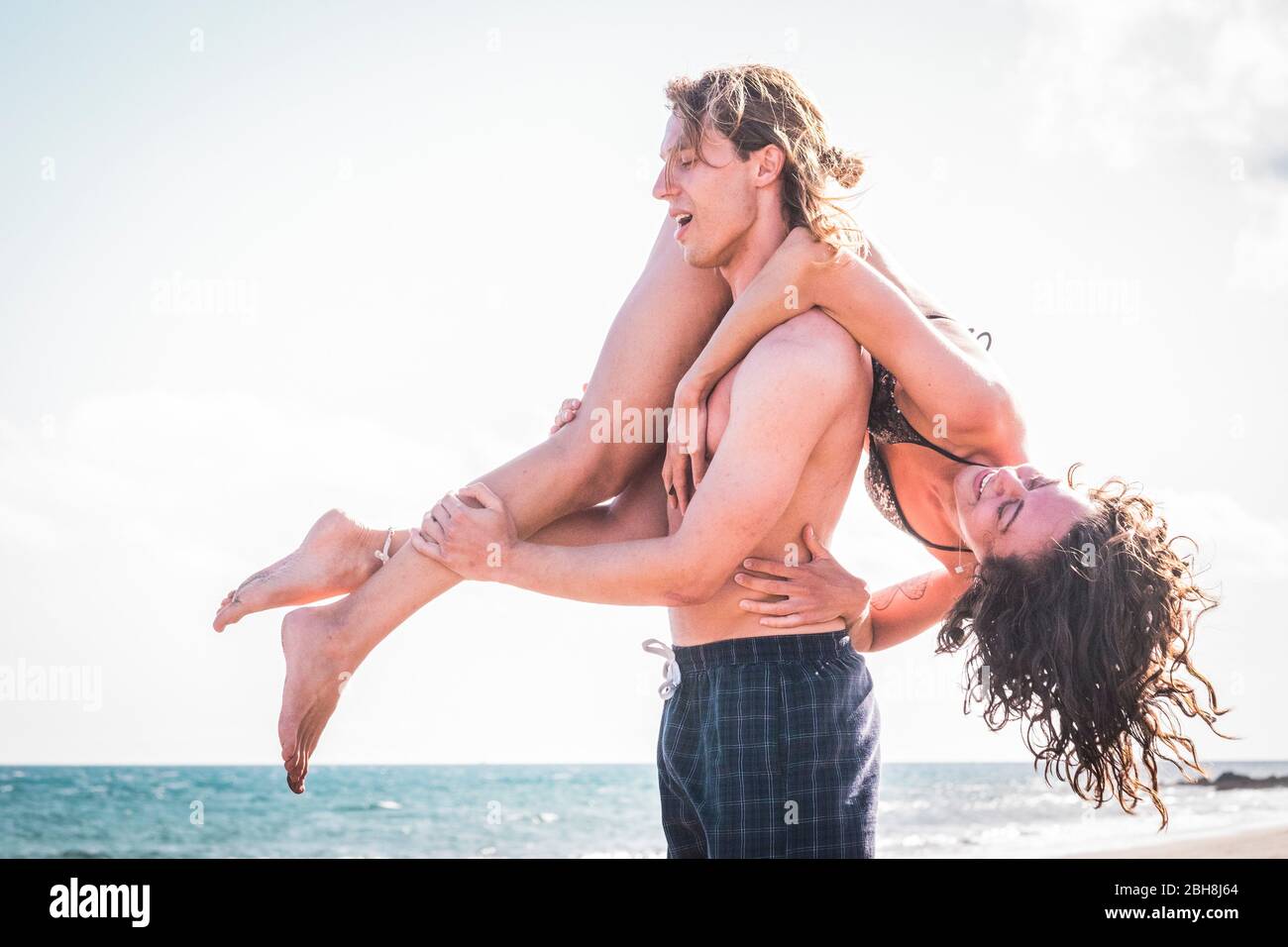 Glücklich fröhlich schöne kaukasische youing Paar genießen und Spaß im Urlaub haben - Mann tragen die Freundin auf dem Rücken und beide lachen viel - Liebe und Beziehung - Menschen im Freien im Sommer Stockfoto