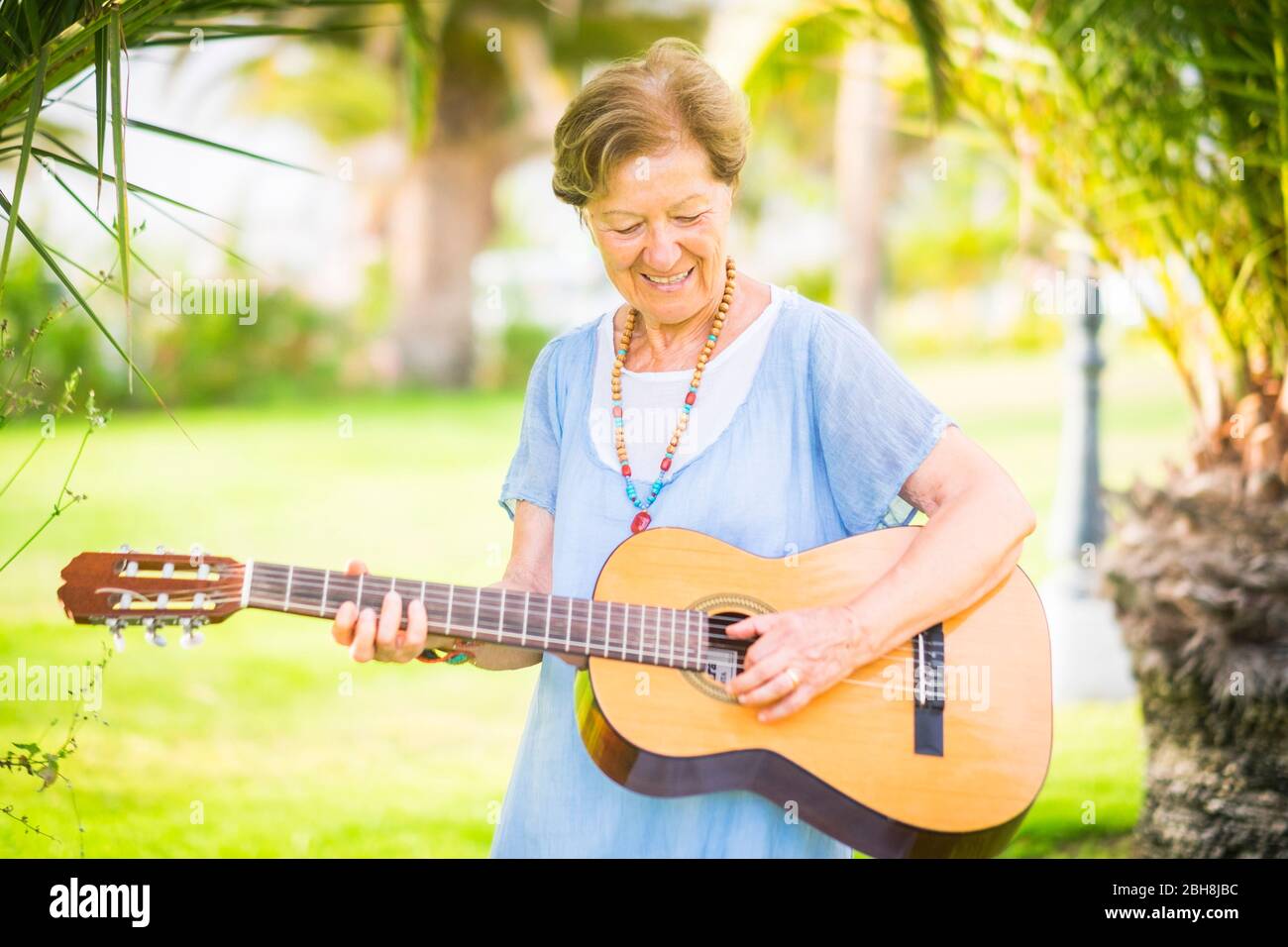 Fröhliche und glückliche alte ältere kaukasische Frau lächelnd und Spaß beim Spielen einer Gitarre und Dong-Musik im Outdoor Park Freizeitaktivitäten - Rentner glückliche Menschen mit Interessen genießen neues Leben Stockfoto