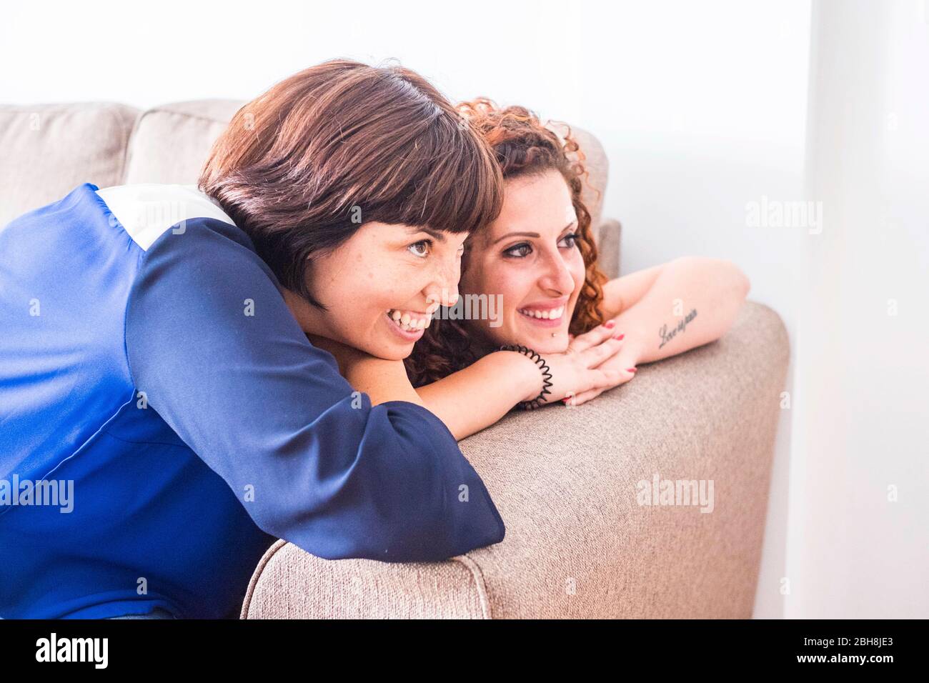 Paar odd zwei Freundinnen bleiben nah zusammen auf dem Sofa lächelnd und Spaß haben. Freundschaft oder Beziehung zu Hause drinnen mit schönen Lifestyle-Art und Weise zu leben Konzept Stockfoto