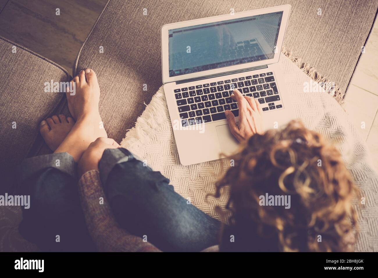 kaukasische Frau in Freizeitkleidung zu Hause, barfuß und komfortabel, tippen Sie auf einem Laptop arbeiten frei und unabhängig - alternative digitla Nomad und Frelance Arbeitsstil - von oben gesehen Stockfoto