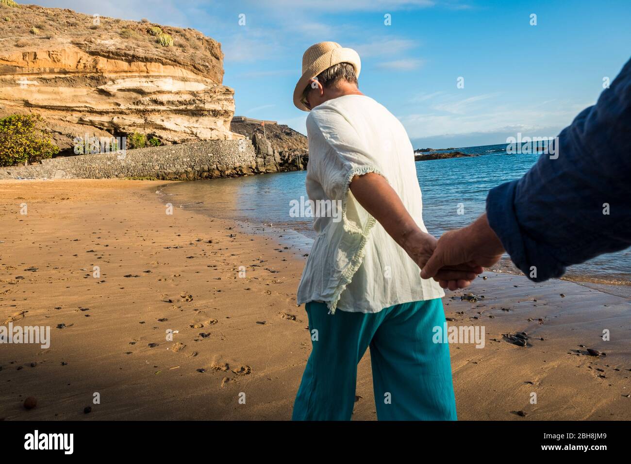 Ältere kaukasische Paar am Strand im Sommer. Freizeitaktivitäten hängend Hände zusammen und Wandern am Ufer. Farben und schöne natürliche Ort und Hintergrund. Hand auf Hand für Liebe Konzept Stockfoto