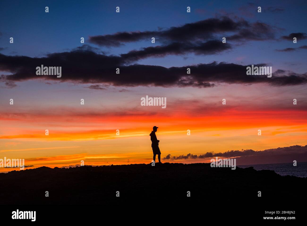 Mann im Freien stehend, der den romantischen Sonnenuntergang genießt - die Natur und das Glück für freien Lebensstil fühlt - Menschen und Outdoor-Show mit farbigen Wolken in der Dämmerung Stockfoto