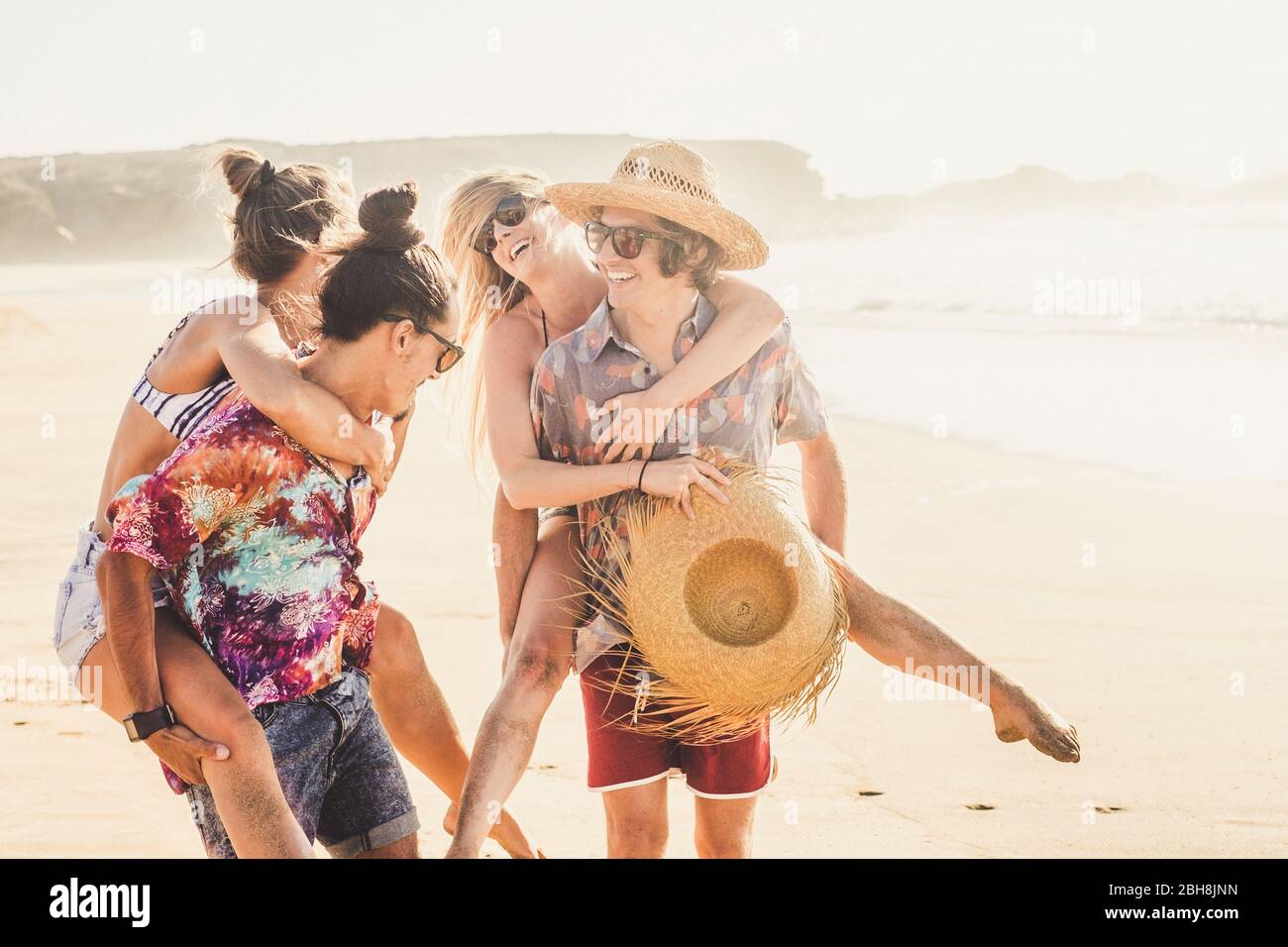 Fröhliche Freunde ein paar Leute Mädchen und Jungen haben gemeinsam Spaß im berach im Sommerurlaub zusammen - Männer tragen die Frauen und alle lachen und lachen viel Stockfoto