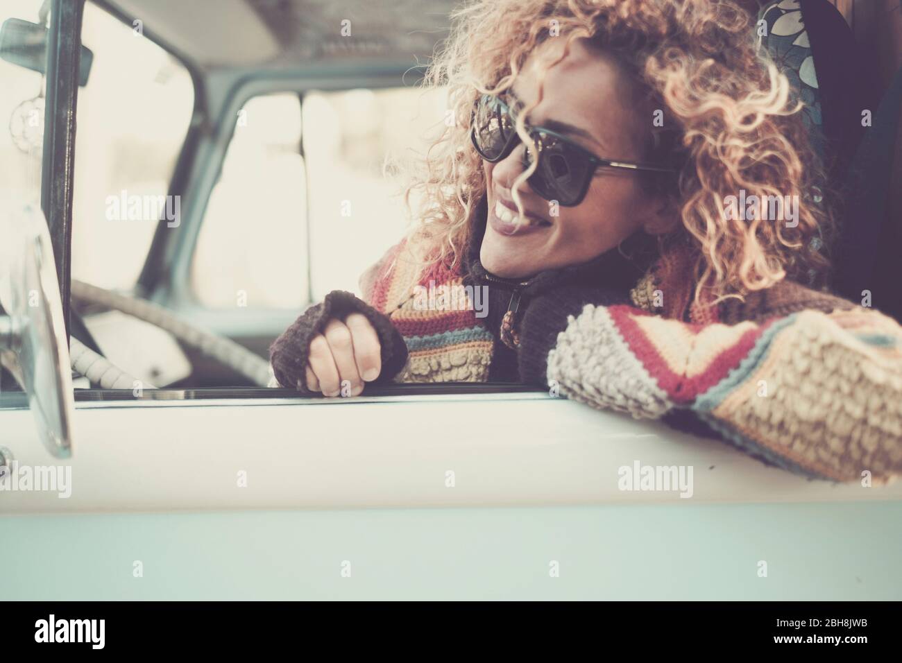 Fröhlich glücklich schöne kaukasische junge Frau suchen und lächeln aus dem Fenster von alten vintage van Bus mit Sonnenbrille - Reise-Fahrkonzept für niedliche attraktive Mädchen mit lockigen Haaren Stockfoto