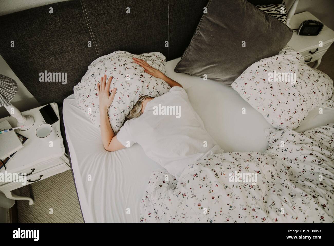 Frau liegt mit Kissen auf dem Kopf im Bett, muss, unausgeschlagen Stockfoto