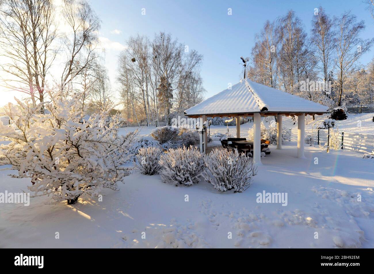 Schneebedeckter Garten mit Pavillon und Sitzecke im Winterschlaf Stockfoto