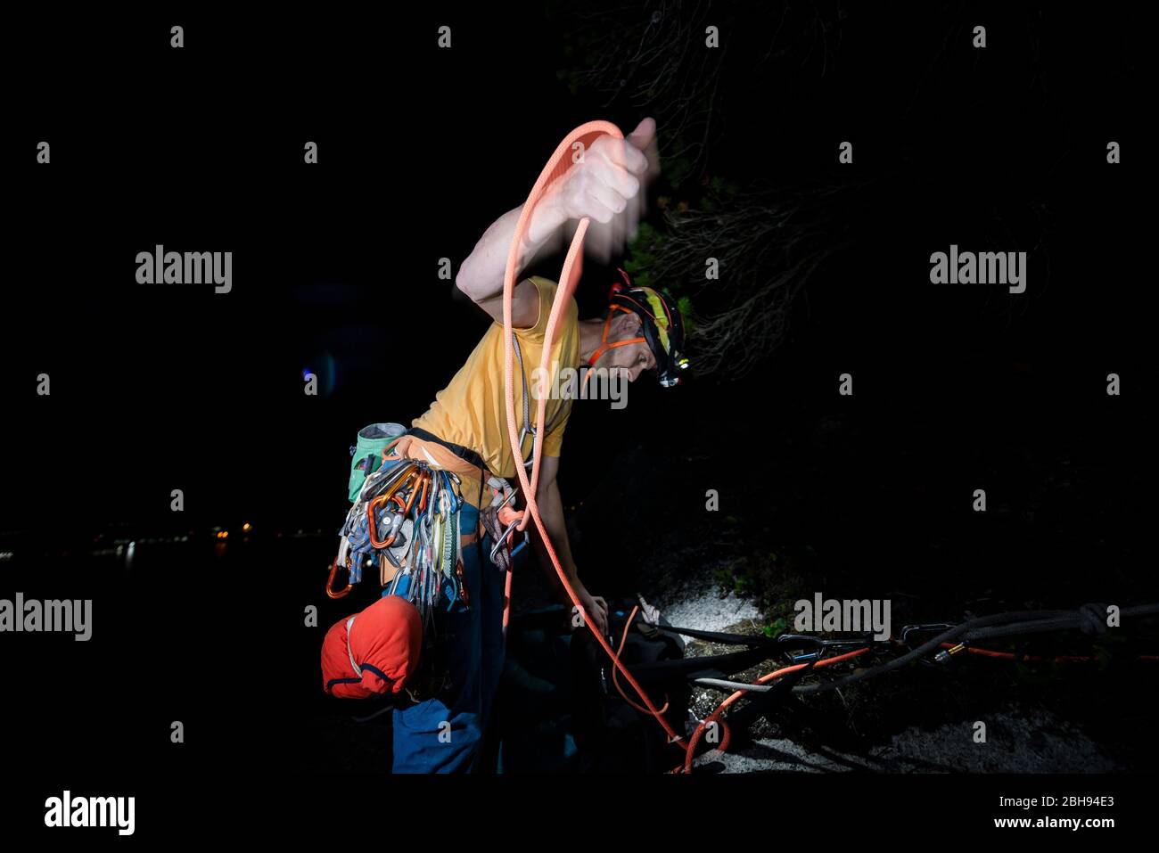 Mann, der Seil nach dem Klettern in der Nacht in der dunklen Stirnlampe aufwickelt Stockfoto