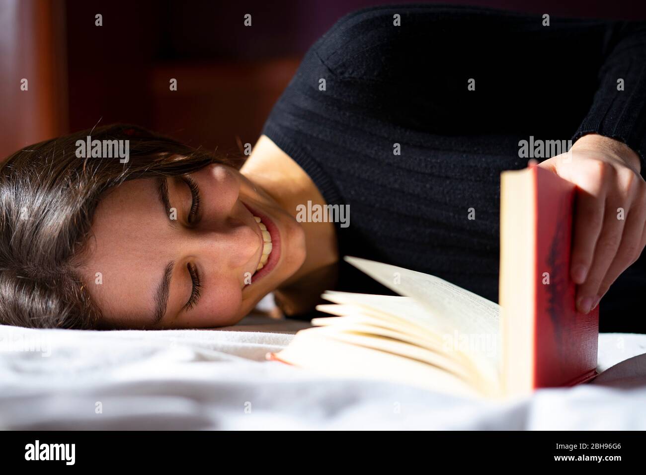 Frau im Bett liegend und ein Buch lesend. Stockfoto