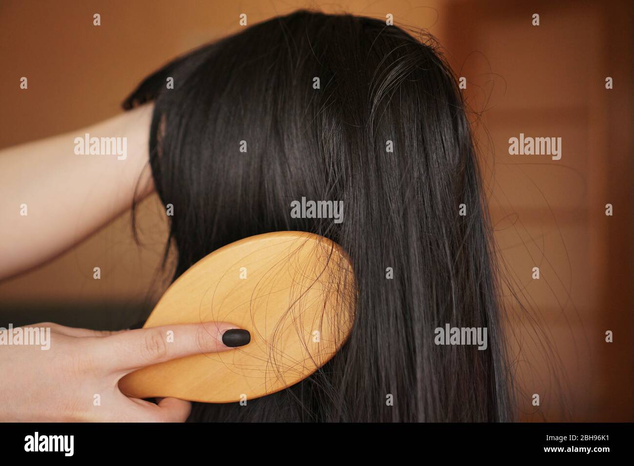 Weibliche Hand hält eine schwarze Perücke mit langen Haaren und Kämme einen Holzkamm. Friseur und Haarpflege Stockfoto