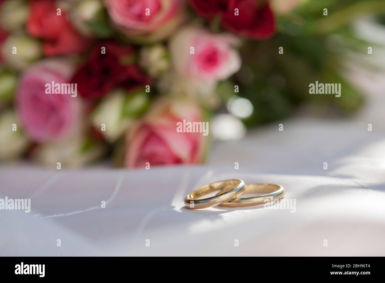 goldene Trauringe vor rosa roten Rosen Bouquet Stockfoto