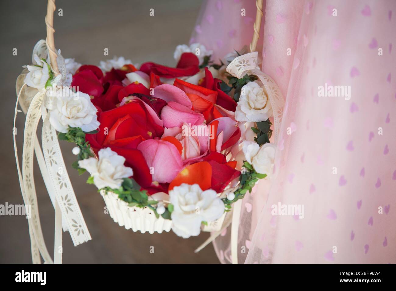 Mädchenhand mit Blumenkorb, rote Rosenblätter Stockfoto