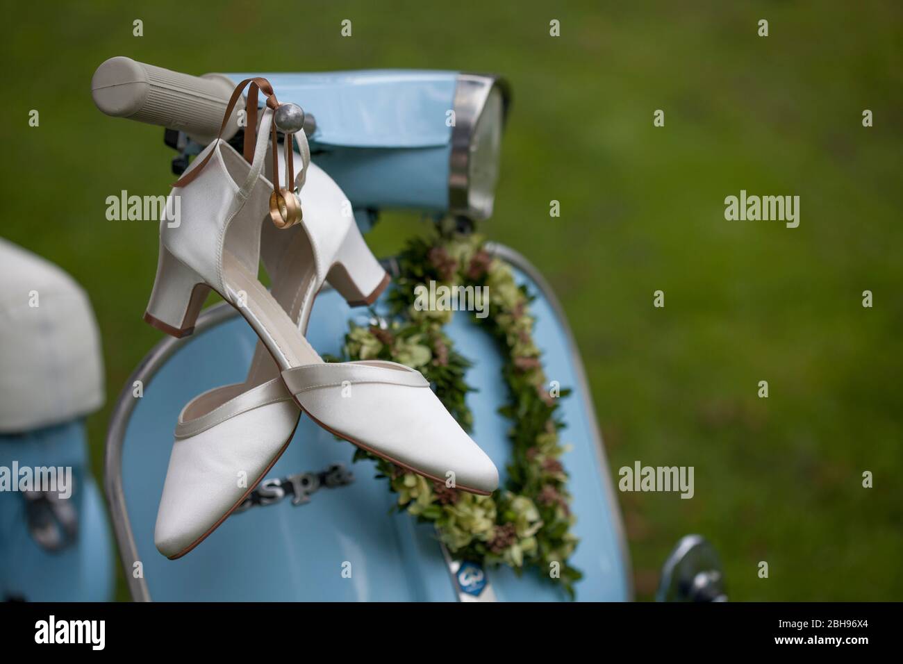 Ringe und Brautschuhe hängen an den Lenkern einer hellblauen Vespa Stockfoto