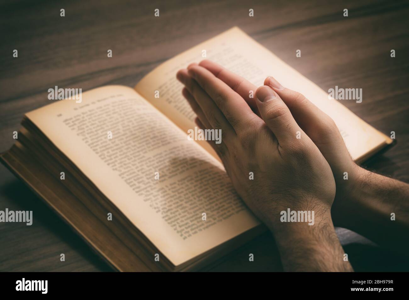 Gebet, Mann überreicht ein offenes Buch Heilige Bibel, hölzerner Schreibtisch Hintergrund. Konzept von Glaube, Religion und Spiritualität Stockfoto