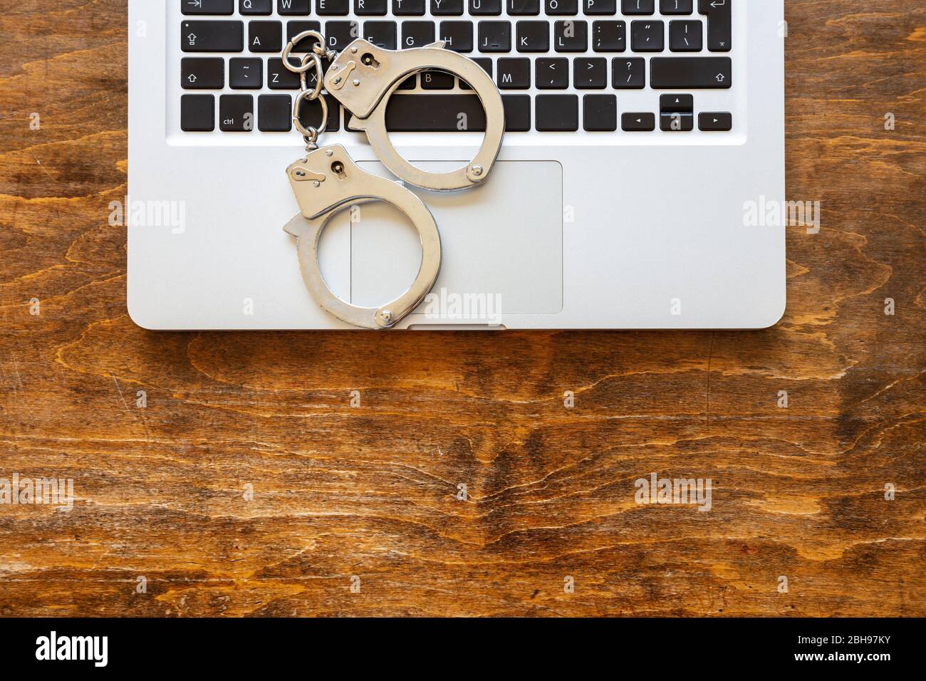 Handschellen auf einem Computer-Laptop, Hintergrund des hölzernen Bürotisches, Draufsicht. Cyberkriminalität, Hacker Arrest Konzept Stockfoto