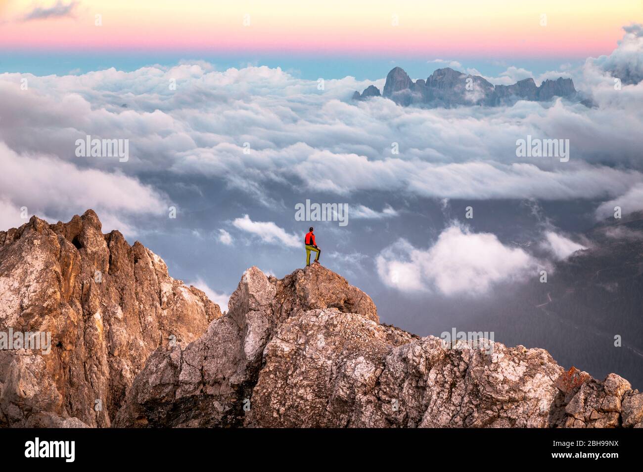 Einsamer Mann steht auf einem Bergrücken, im Hintergrund ein Wolkenmeer rund um die Agner Bergkette, Pale di San Martino Gruppe, Blick vom Costabella-Grat, Dolomiten, Italien Stockfoto