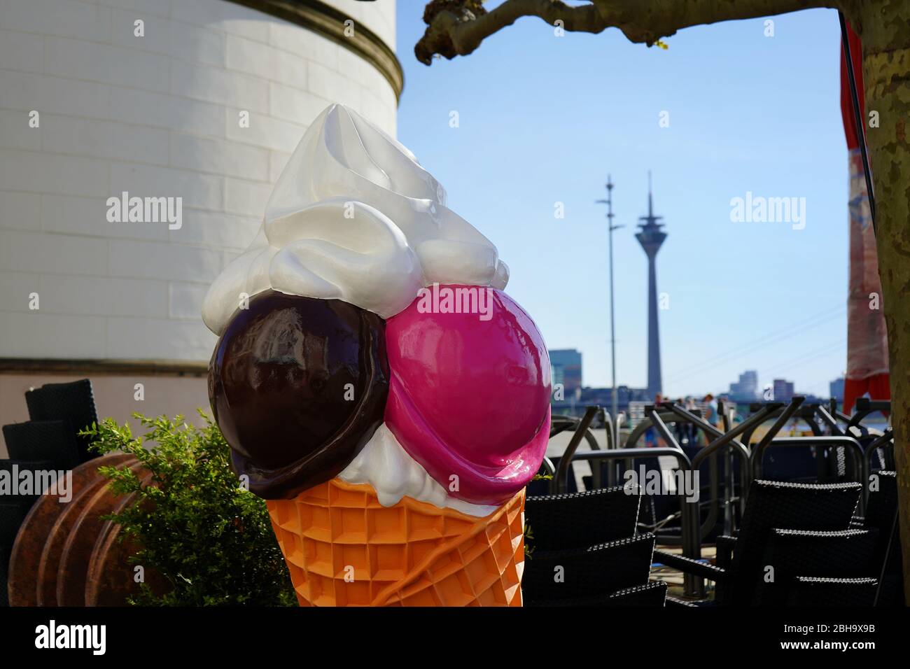 Hintergrundfoto mit selektivem Fokus auf einem Eiskegel vor einem leeren Café am Düsseldorfer Rhein. Rheinturm im verschwommenen Hintergrund. Stockfoto