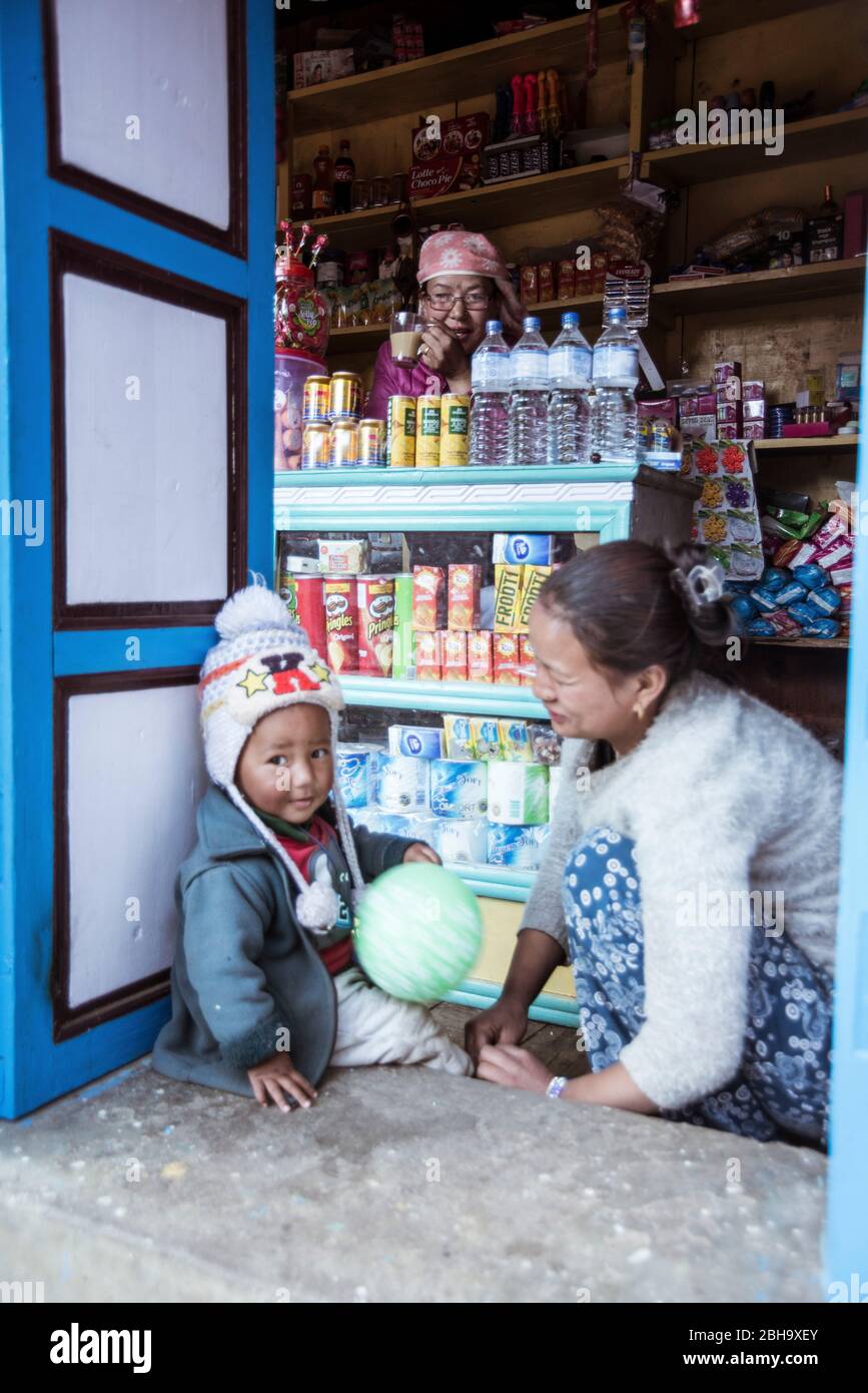Schop in Namche Bazar mit 3 Personen, Junge sitzt mit Mutter vor dem Laden, Großmutter im Hintergrund Stockfoto