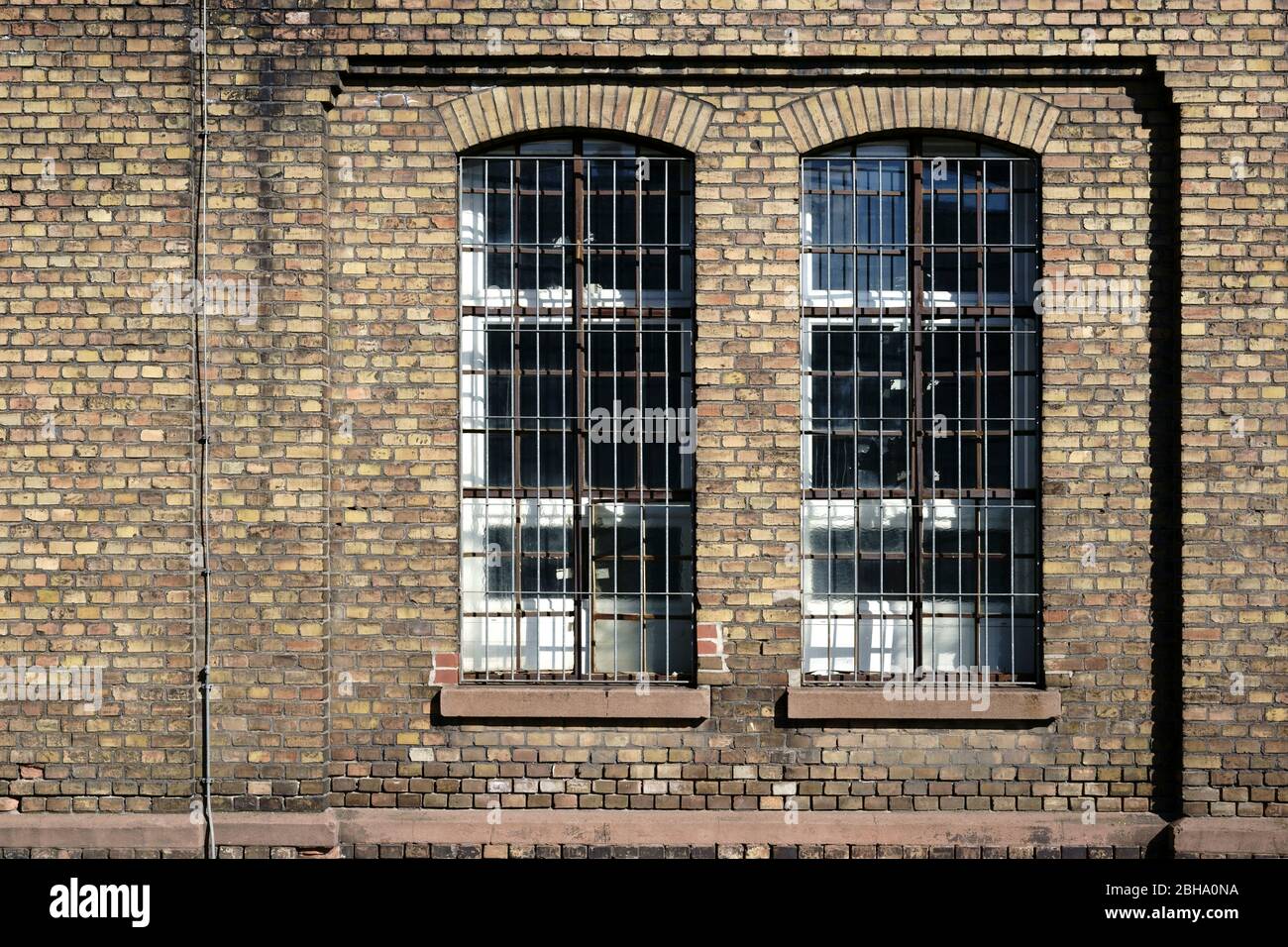 Eine Mauer auf dem stillgelegten Industriegelände von einer alten Fabrik mit einem vergitterten Fenster. Stockfoto