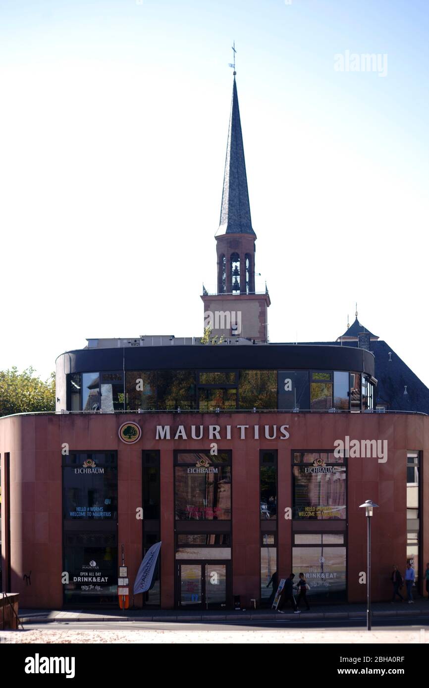 Worms, Deutschland, das moderne Gebäude des Mauritius-Restaurants am Wormser Dom mit dem Turm der Magnuskirche im Hintergrund Stockfoto