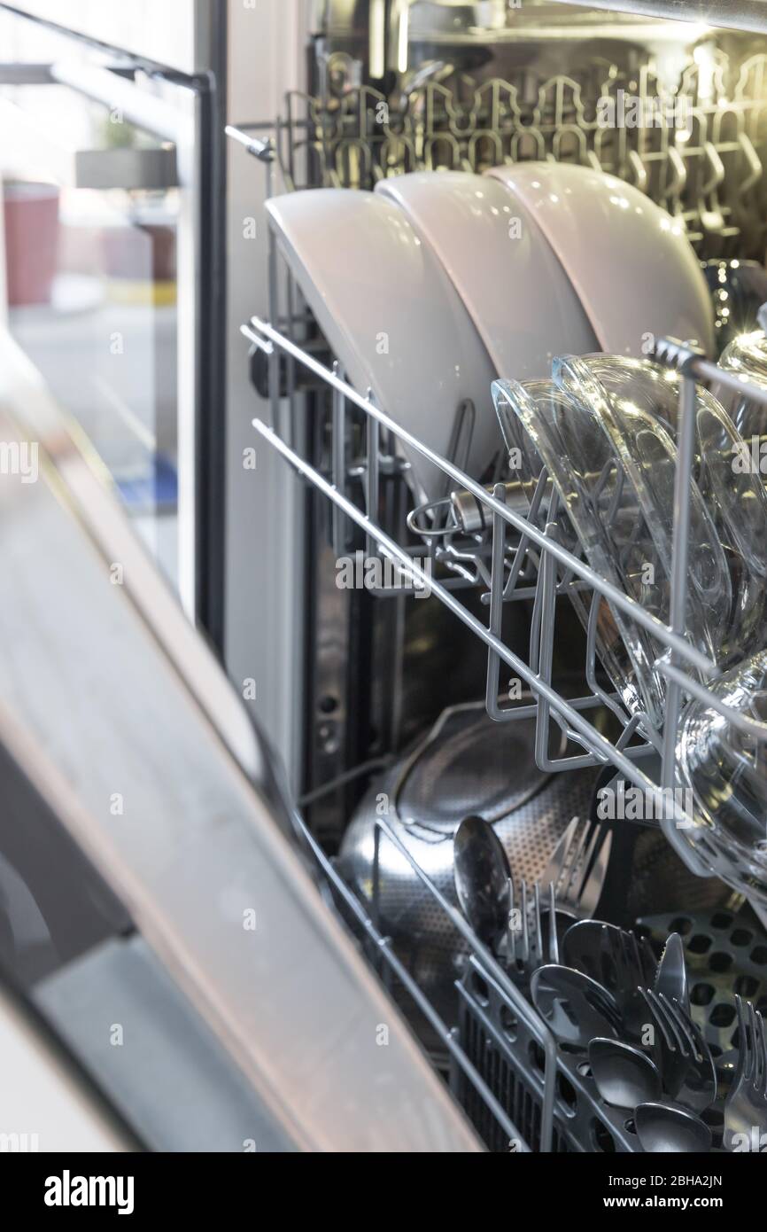 Offene Spülmaschine mit sauberem Geschirr in einer weißen Küche, weiche Konzentration auf Teller und Besteck. Stockfoto