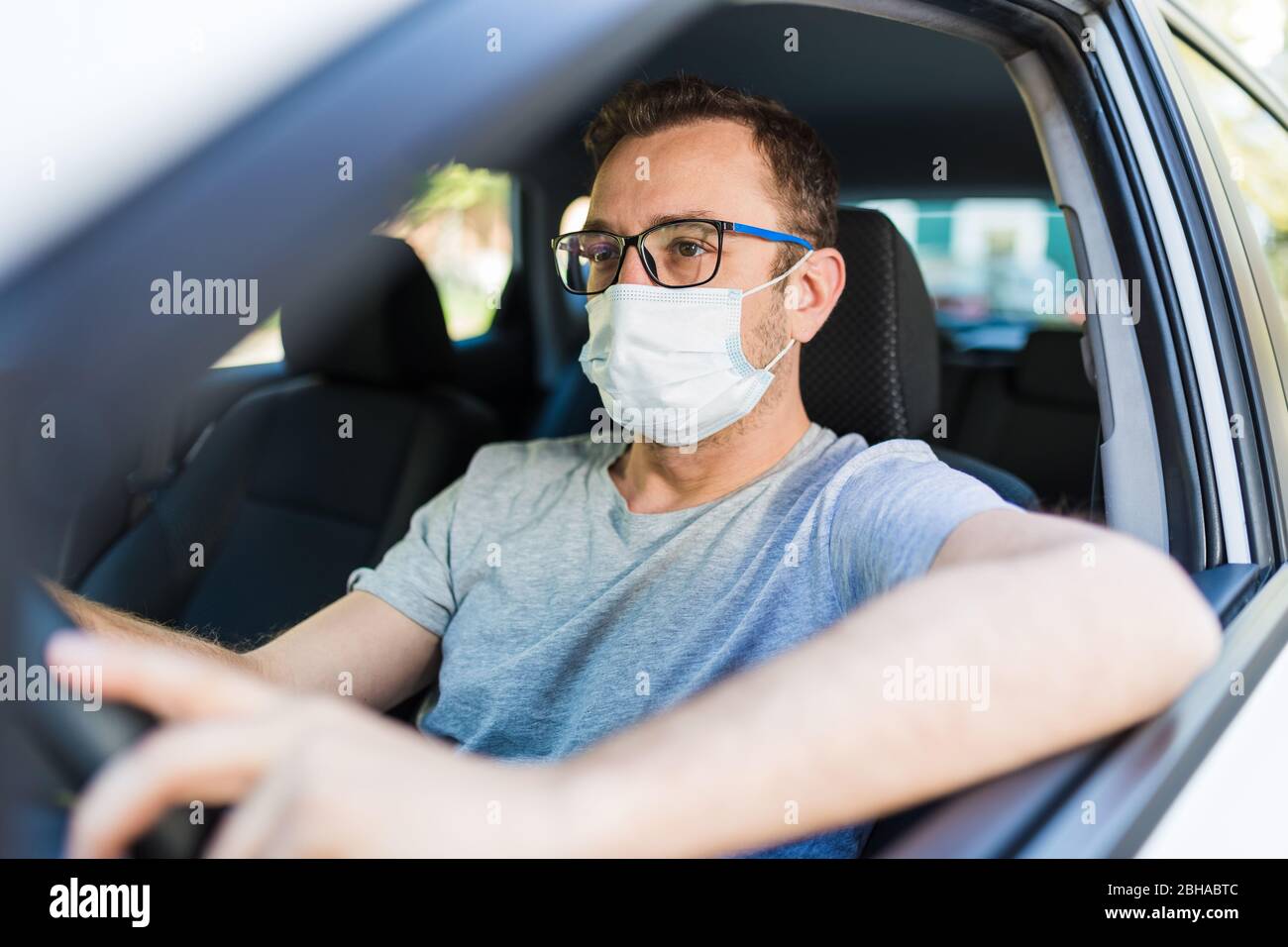 Porträt des Mannes trägt chirurgische Maske während der Fahrt ein Auto. Stockfoto
