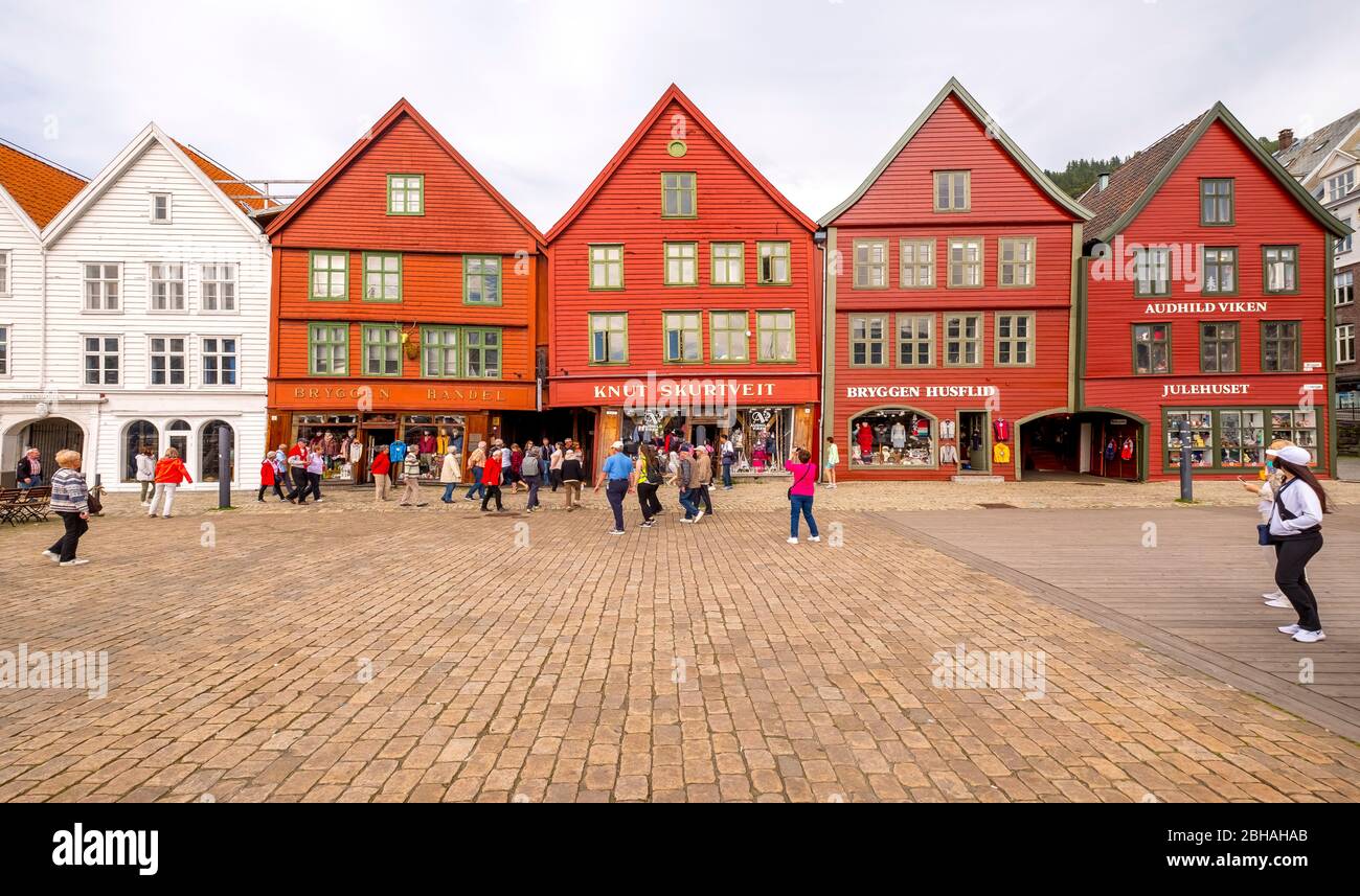 Touristen spazieren auf einem großen gepflasterten Platz vor der Kulisse von bunten Holzhäusern im Hanseviertel Bryggen, Torget, der Deutschen Werft, Bergen, Hordaland, Norwegen, Skandinavien, Europa Stockfoto