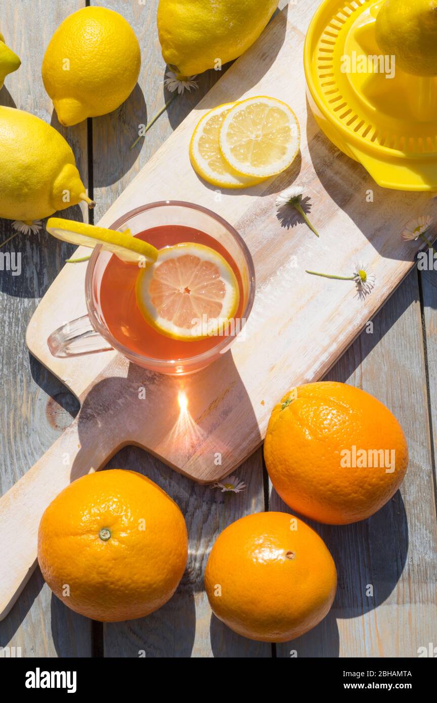 Eine Tasse Zitrusfruchttee, Zitronen und Orangen in der Morgensonne auf Holzhintergrund Stockfoto