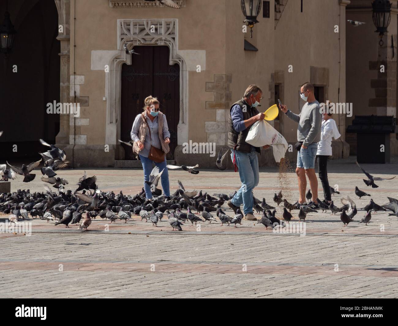 Krakau/Polen - 22/04/2020. Fütterung von Tauben auf dem Hauptplatz von Krakau während der Covid-19 Coronavirus Pandemie. Kein Tourist, Bewohner sind in Masken Stockfoto