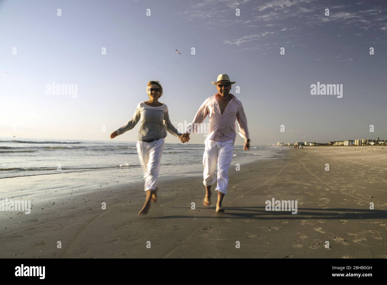 Paar in maritimer Kleidung, die im Surfgebiet des einsamen Strandes von Daytona Beach überlaufen und freundlich in der Kamera aussehen Stockfoto