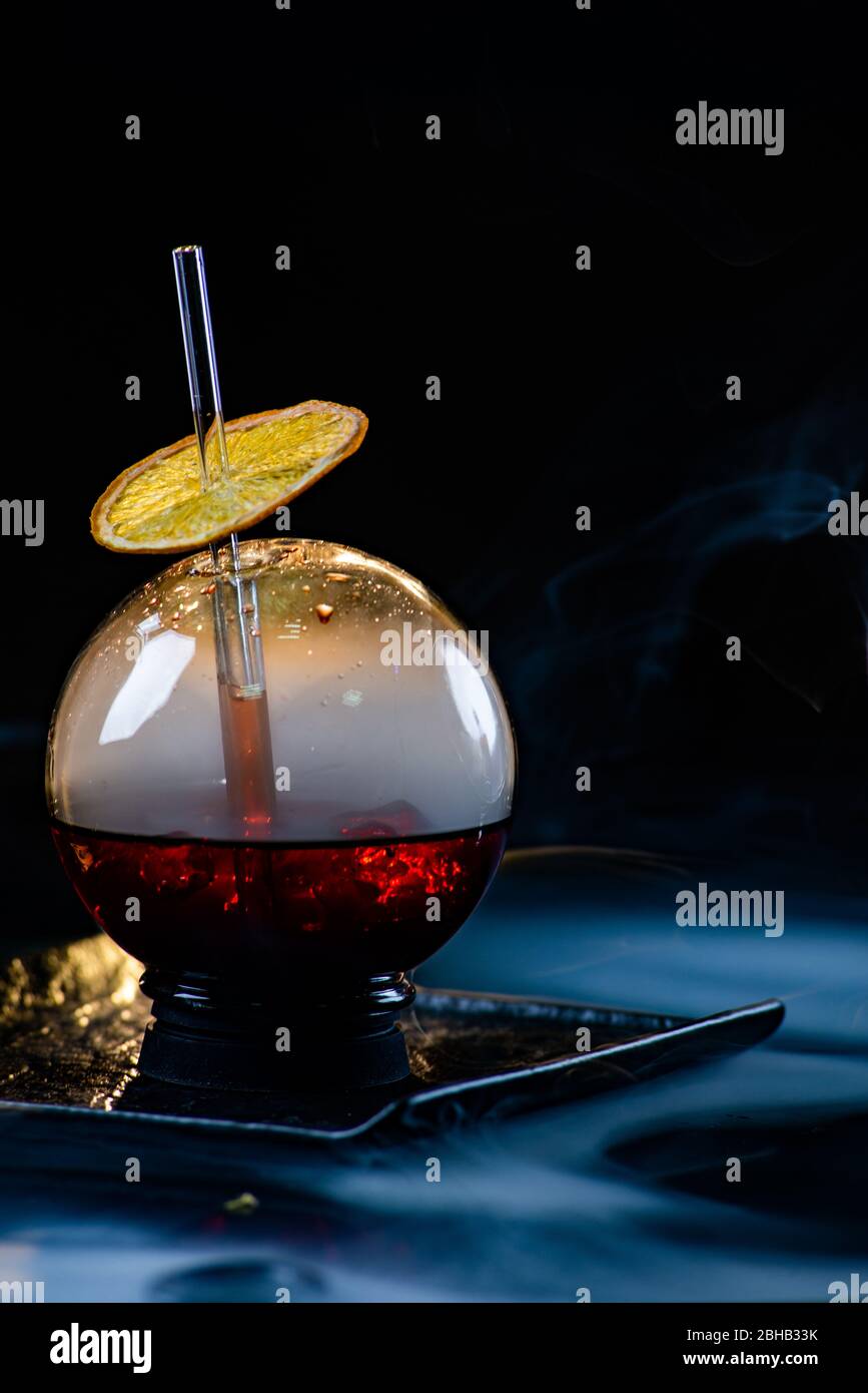 Kugelglas mit Rauch und Alkohol. Karamellisierte Zitronenscheiben. Rauch auf schwarzem Hintergrund. Stockfoto
