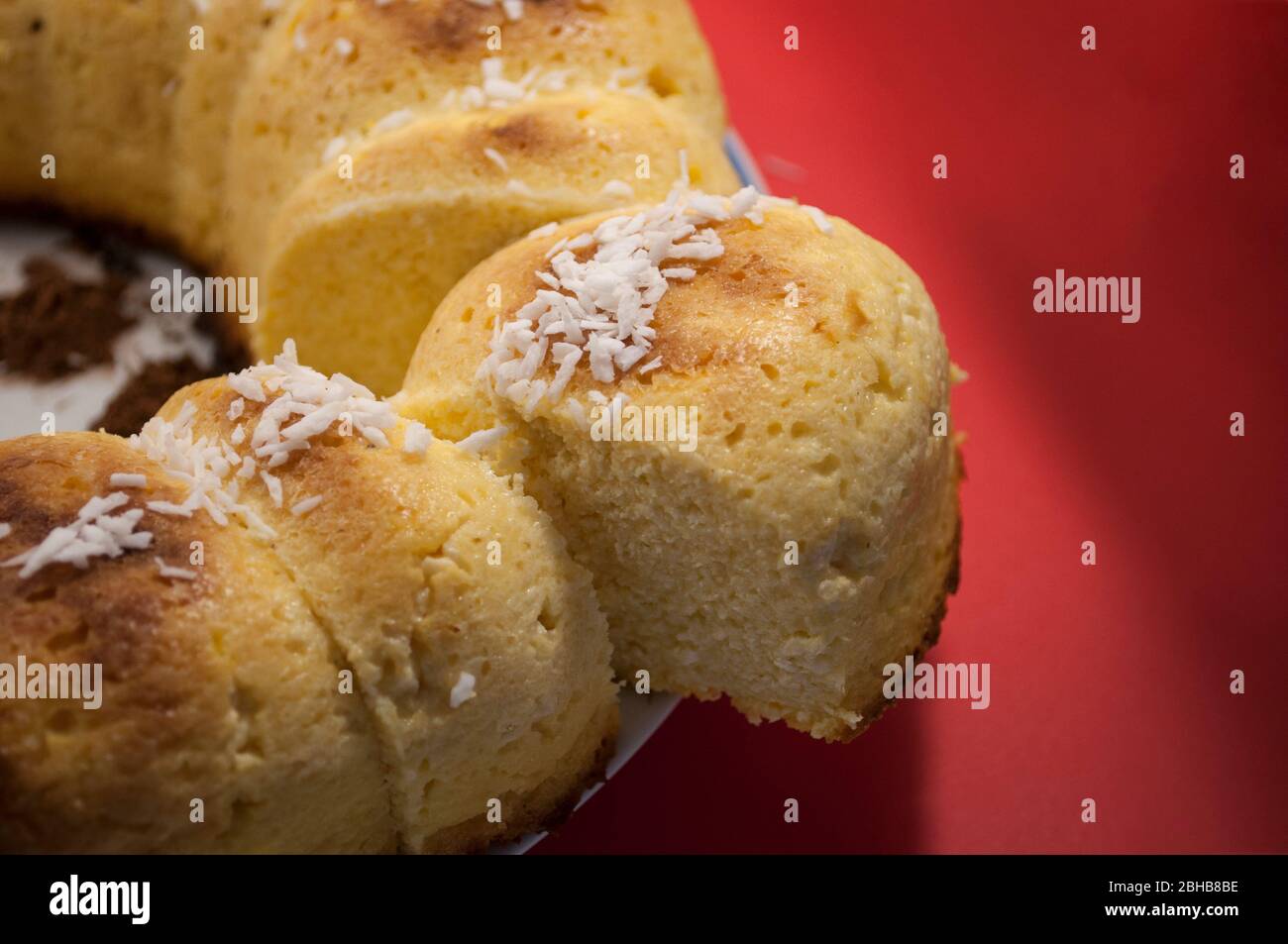 Hausgemachter Käsekuchen mit Kokosflocken auf Teller auf rotem Hintergrund (selektiver Fokus; Nahaufnahme) Stockfoto