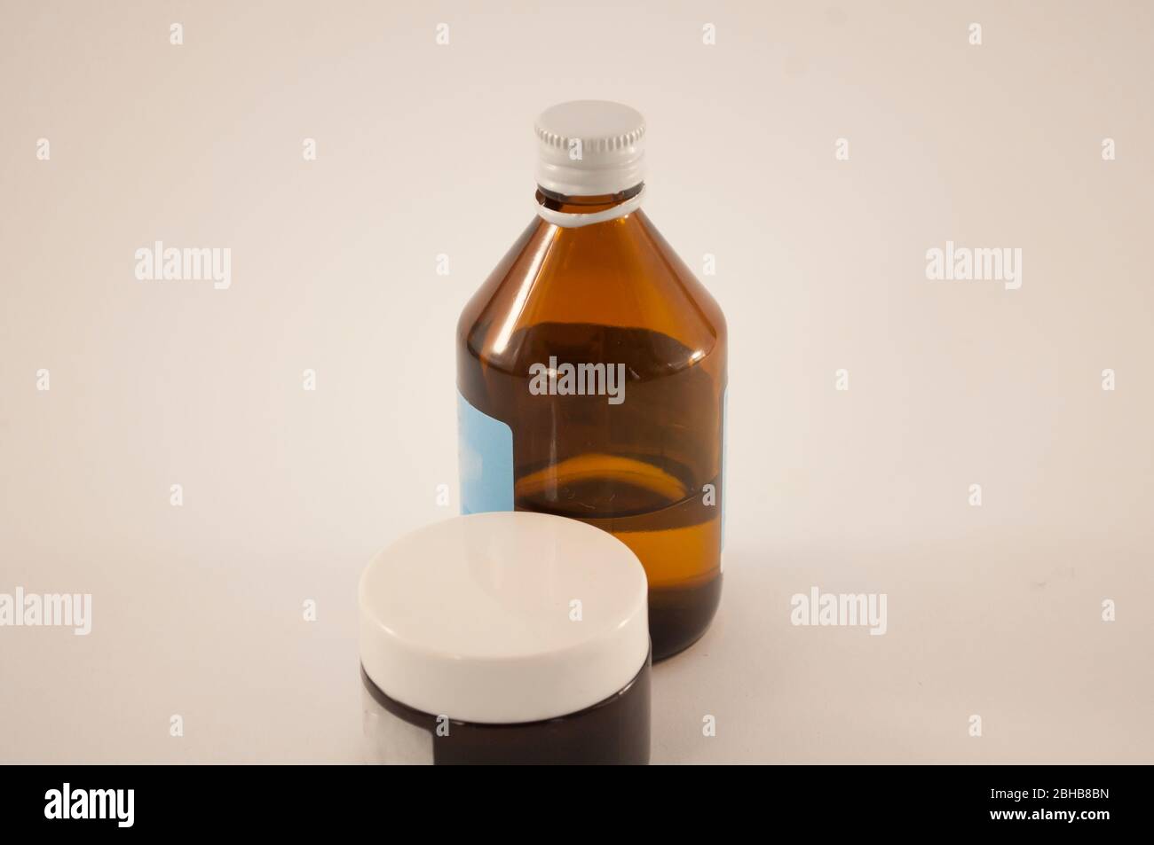Glasgefäß mit weißem Kunststoffdeckel in der Nähe Glasflasche mit flüssigem und blauem Etikett Stockfoto
