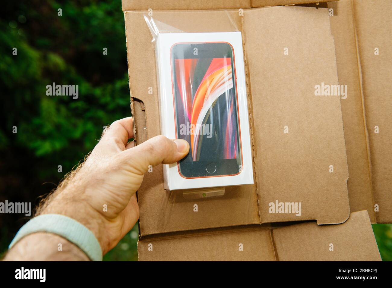 Paris, Frankreich - Apr 24, 2020: Mann hodling Paket mit neuen Budget iPhone SE von Apple Computers Touch ID, Single-Objektiv Rückkamera und iPhone 8 Design mit Interna ab 11 Pro-Version Stockfoto